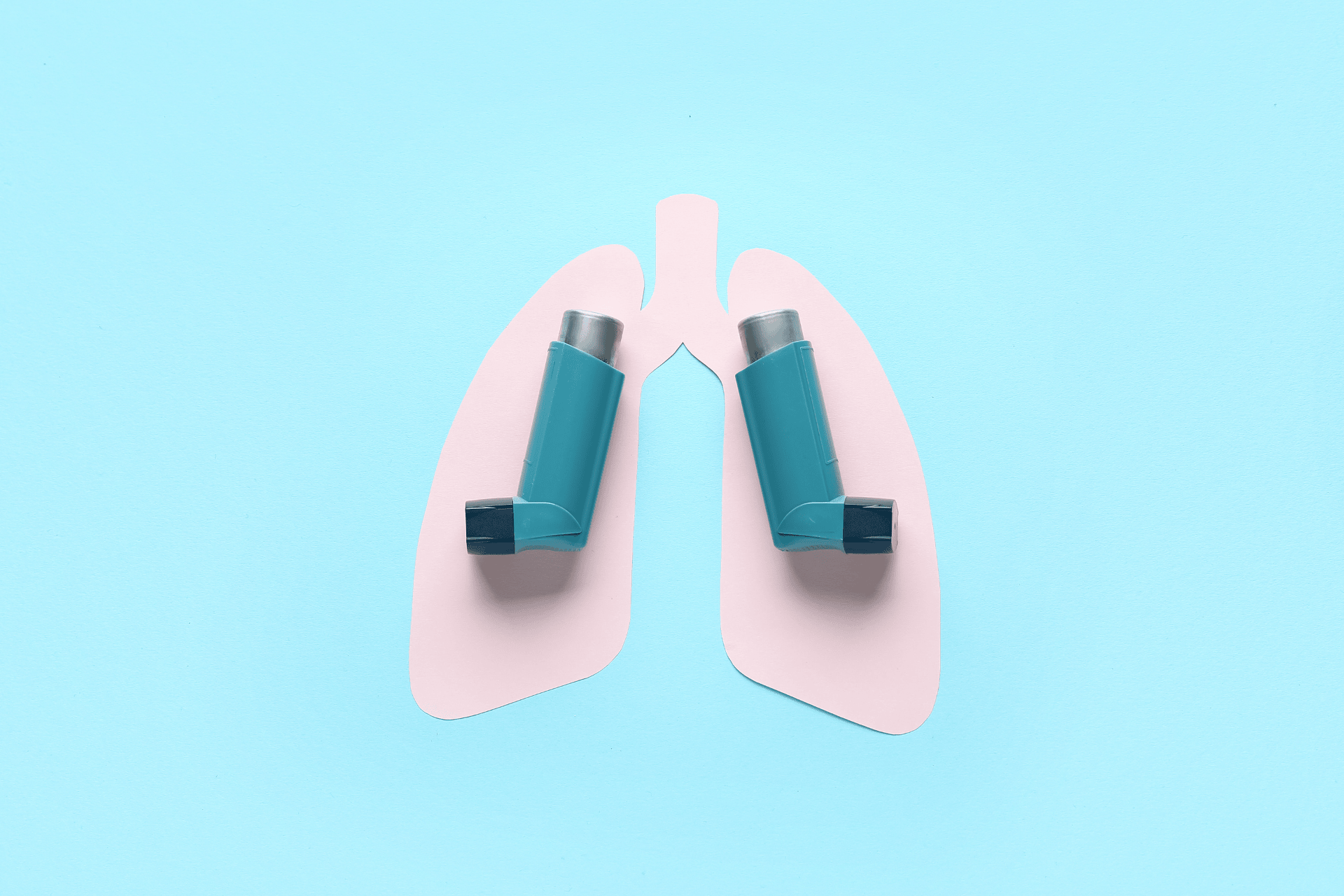 Two asthma inhalers placed on top of a paper cutout shaped like lungs.