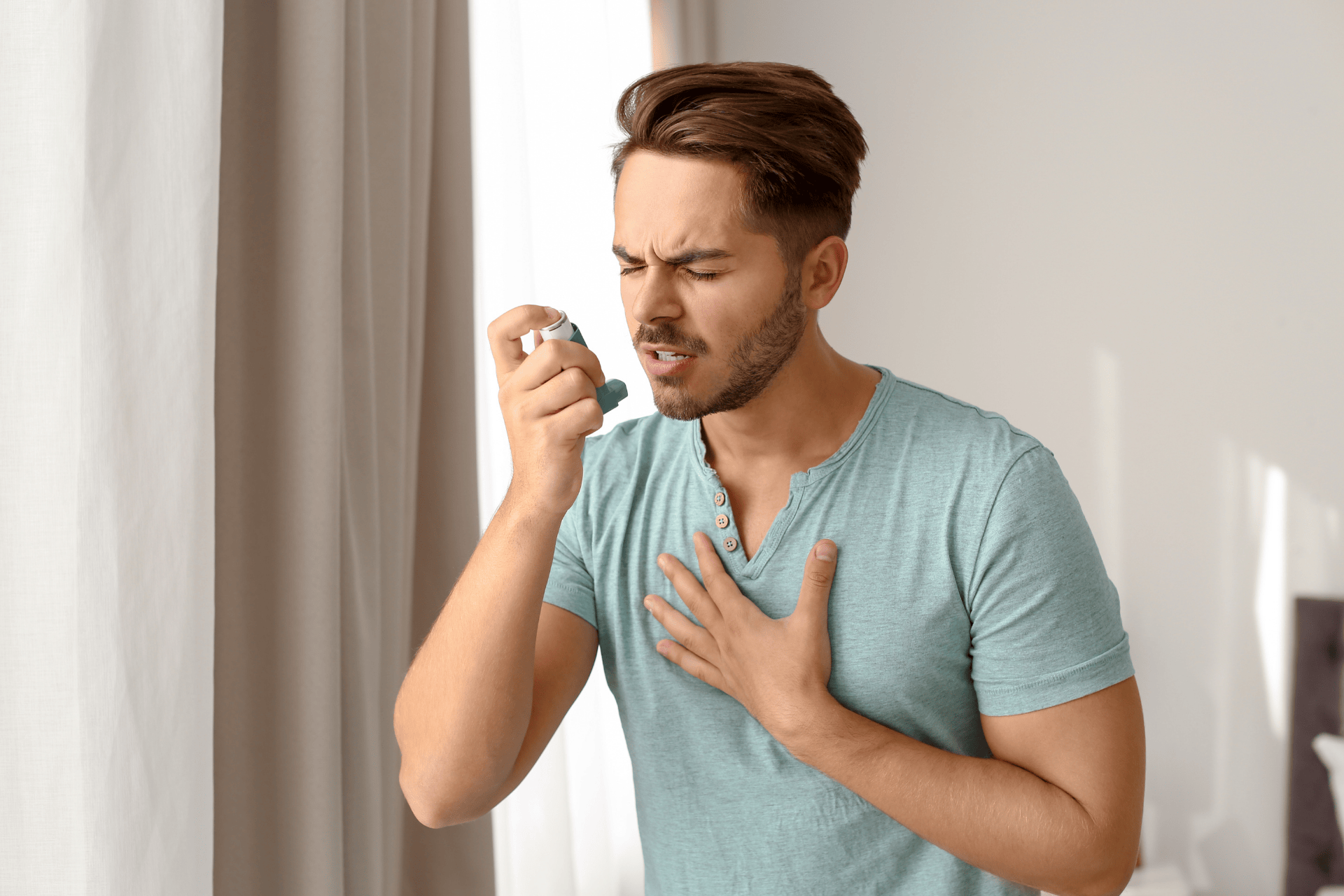 Man clutching his chest while using an asthma inhaler.