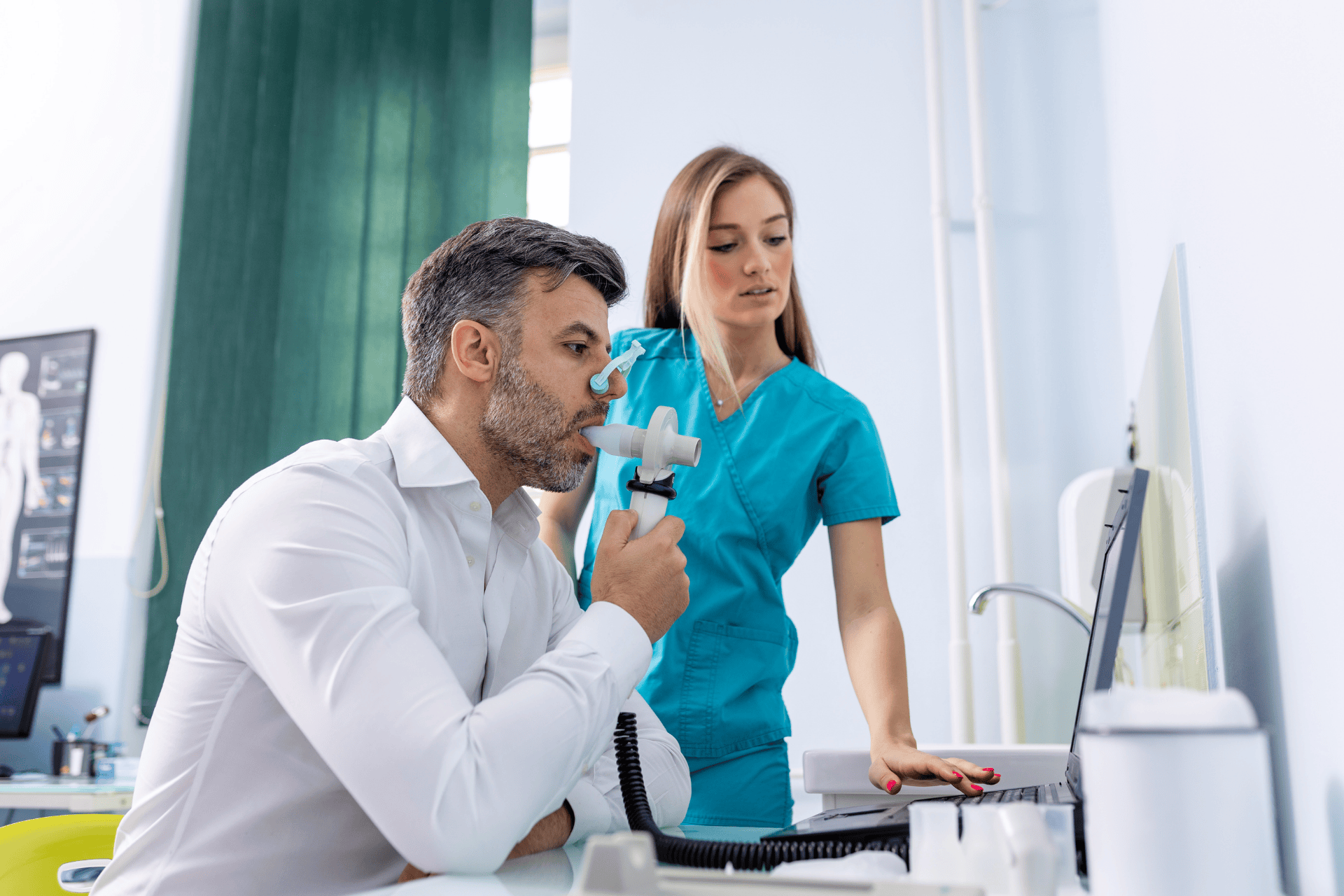Man performing a breathing test with a spirometry device while a healthcare worker monitors the results.