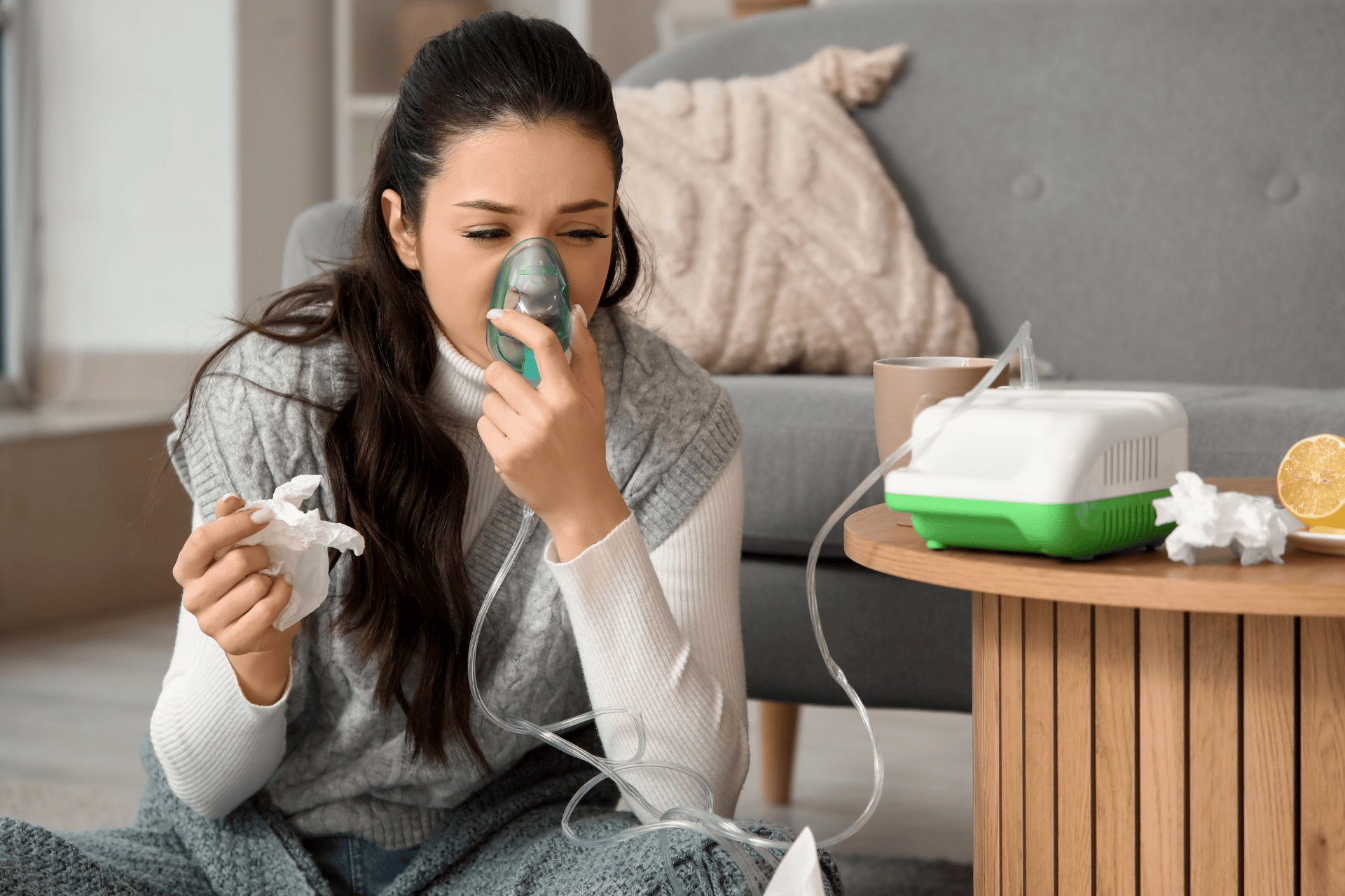 Woman using a nebulizer at home while holding a tissue.