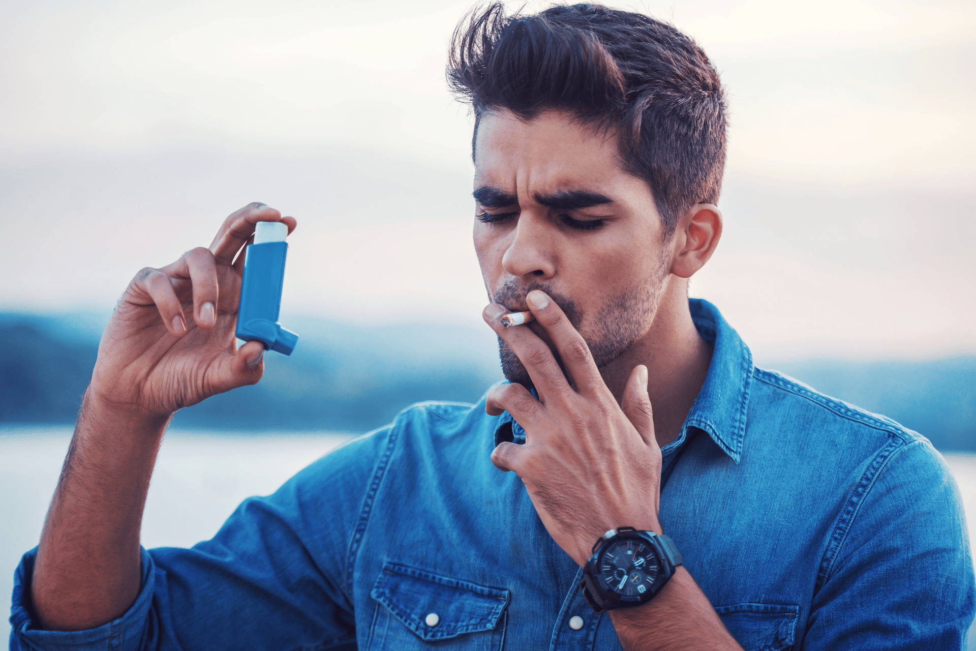 Man smoking a cigarette while holding an asthma inhaler.