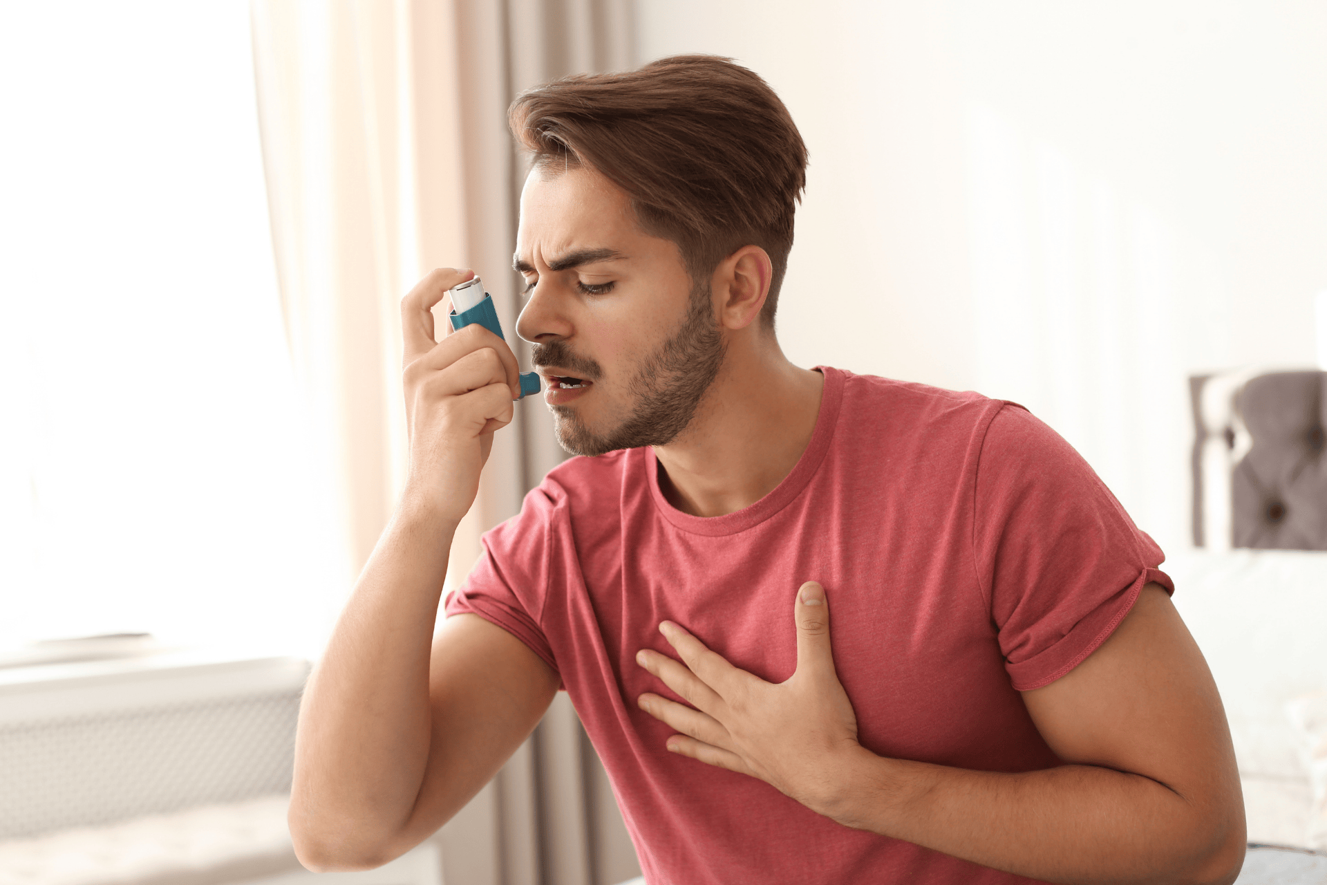 Man holding his chest while using an asthma inhaler indoors.  Choosing the Right Maintenance Inhaler