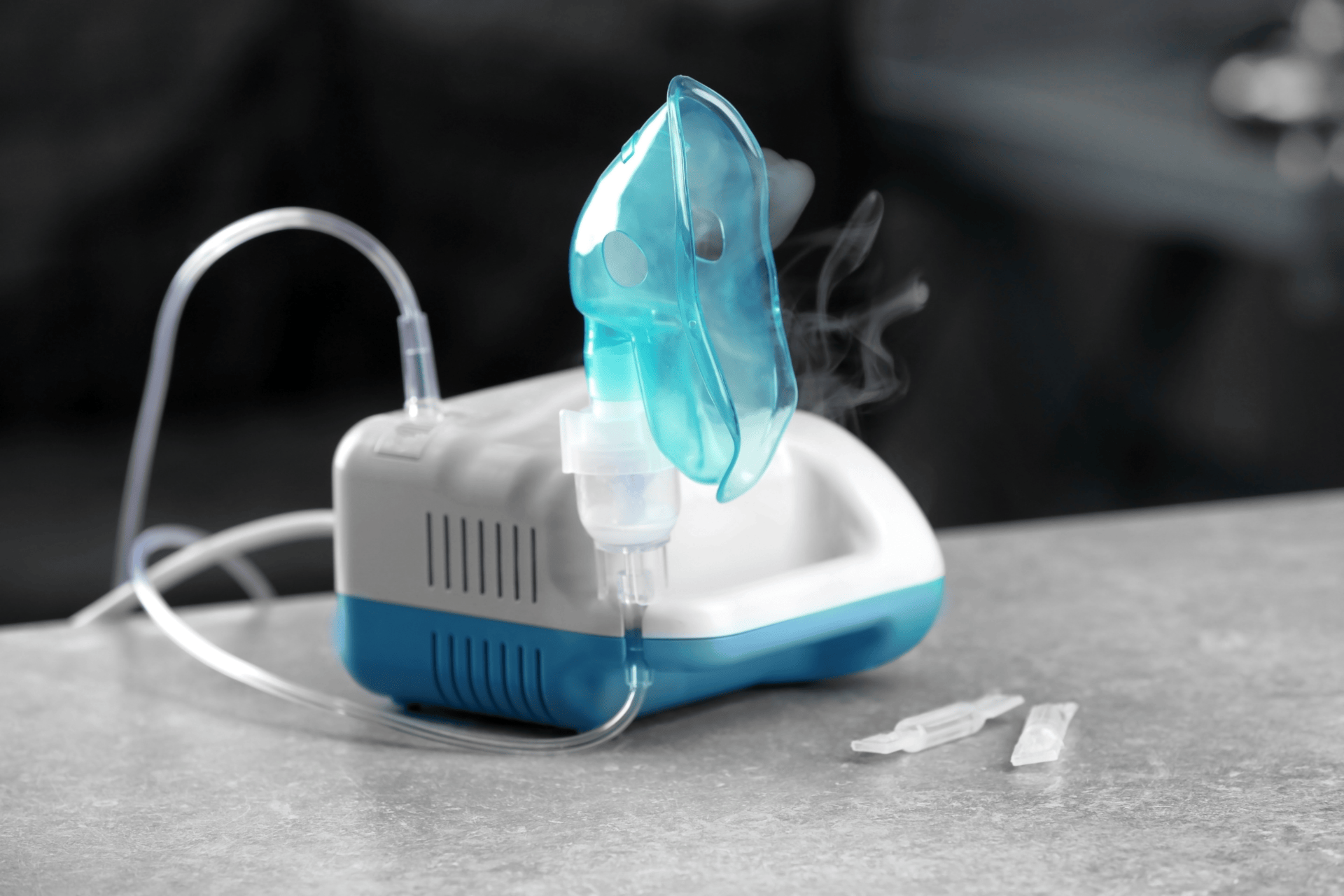 Nebulizer machine with a blue face mask releasing visible mist on a table.