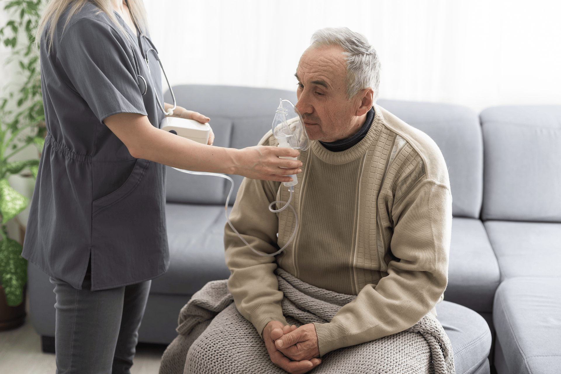 Healthcare worker assisting an older man with a nebulizer mask while he sits on a couch.