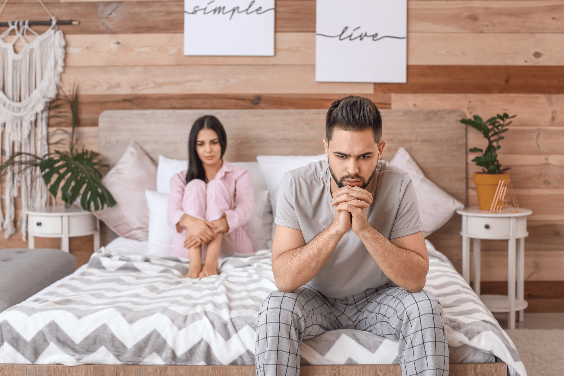 Upset couple sitting on a bed, man looking distressed.