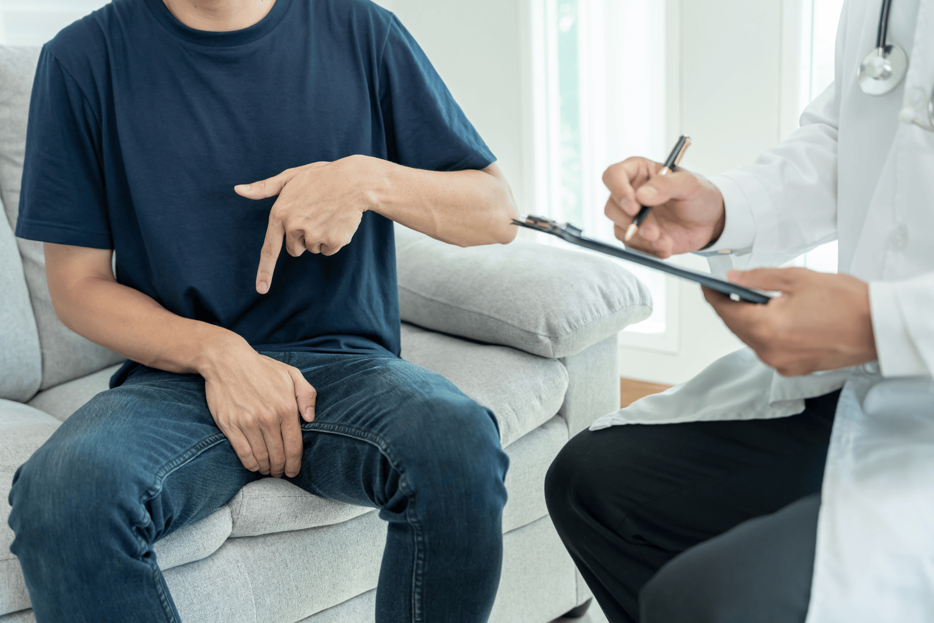 Man pointing to his groin area while speaking with a doctor during a medical consultation.