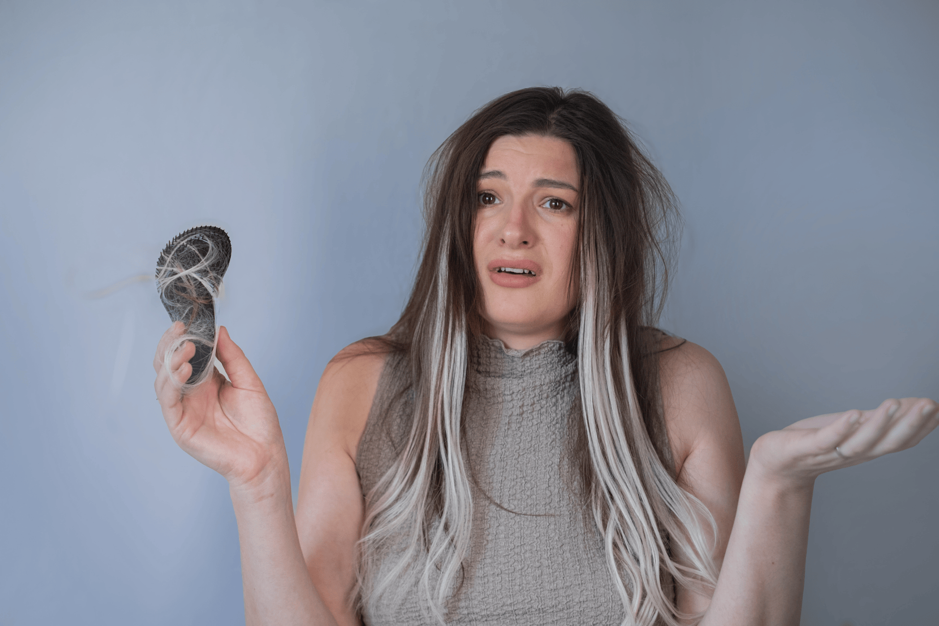 Woman looking distressed while holding a hairbrush full of shed hair, suggesting stress-related hair loss.