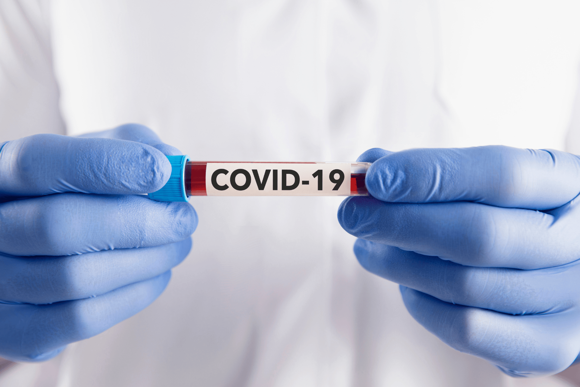 Gloved hands holding a blood sample tube labeled “COVID-19.”