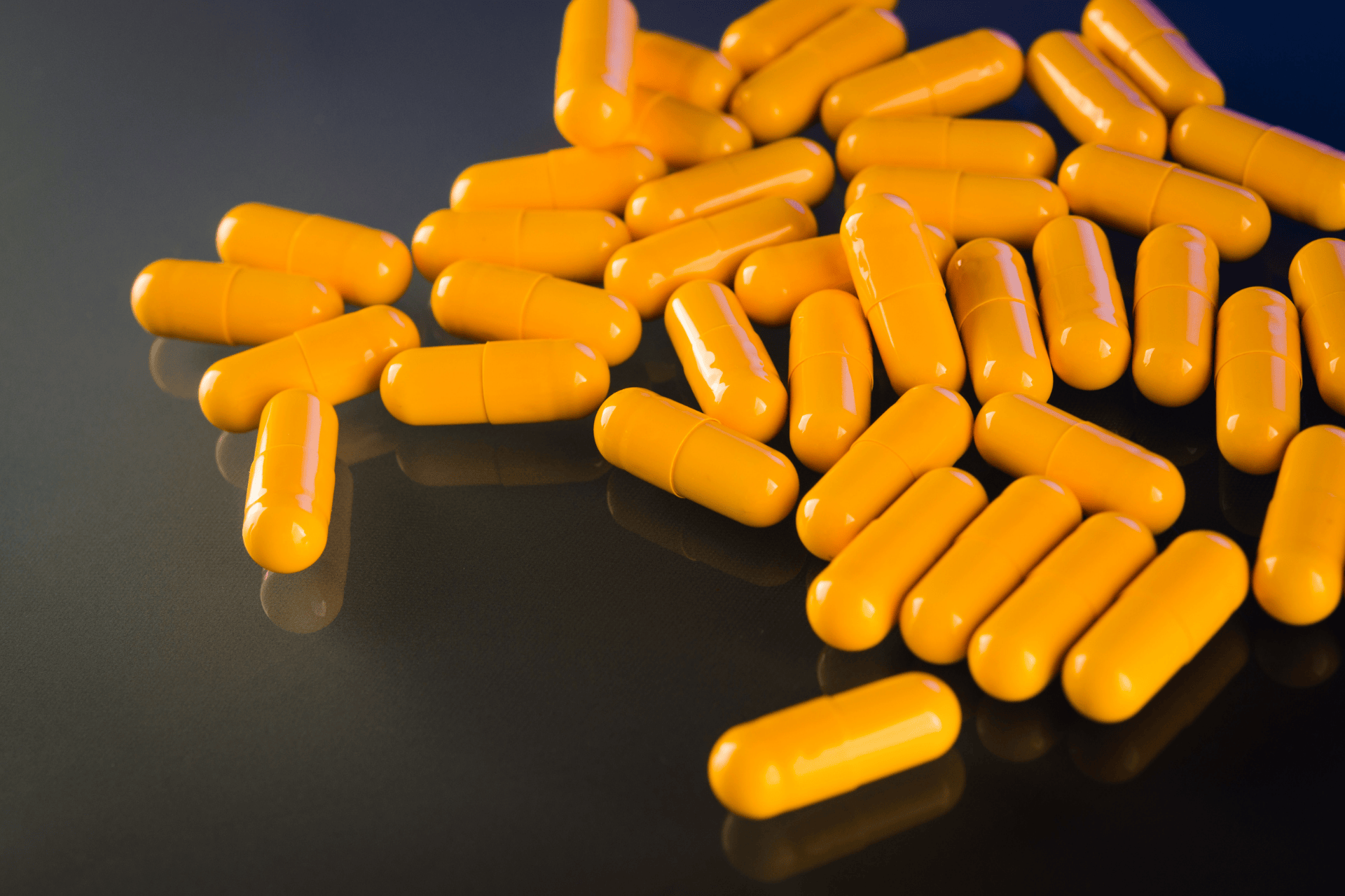 Pile of bright yellow capsules scattered on a reflective dark surface.