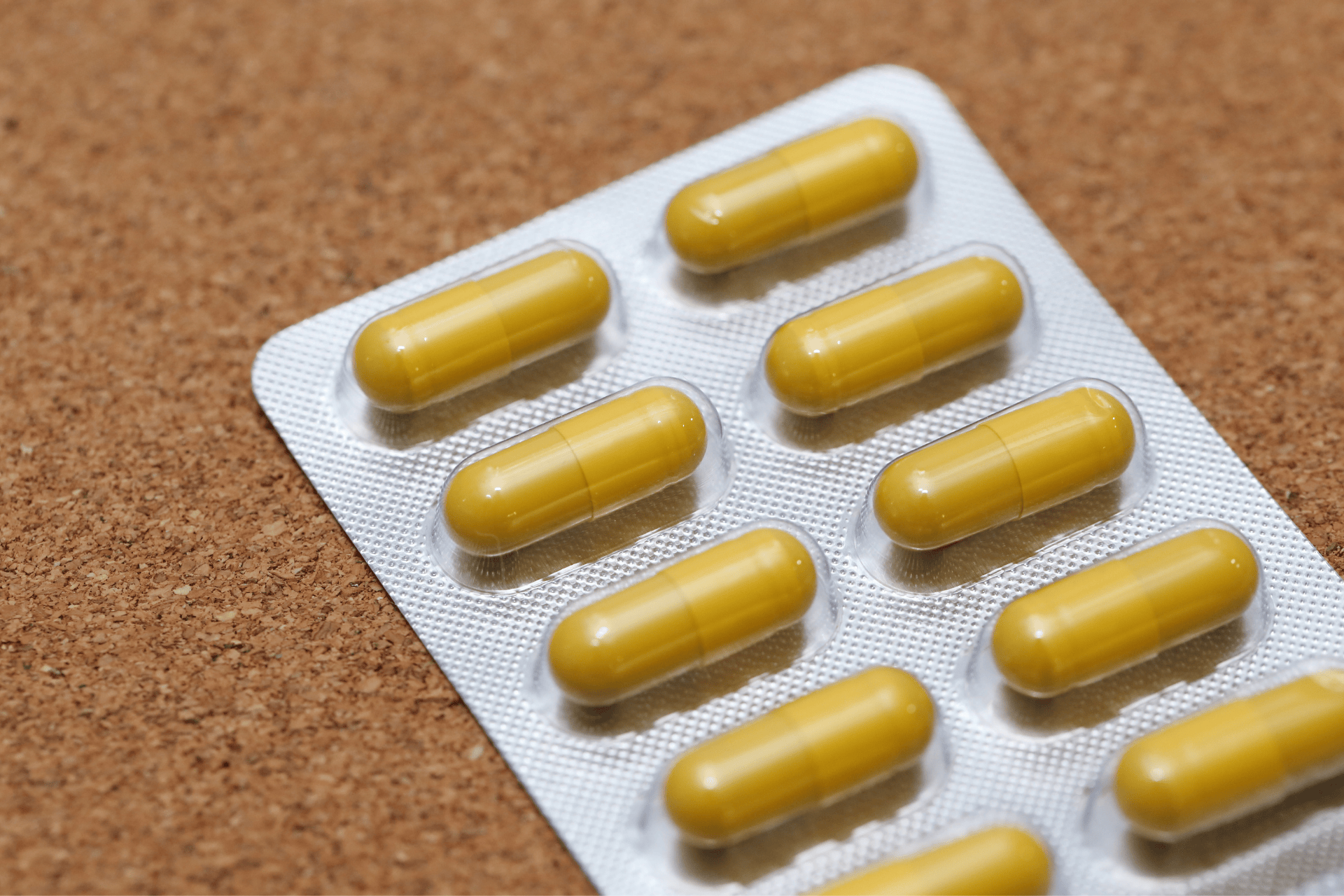 Close-up of a blister pack containing yellow capsules on a cork surface.