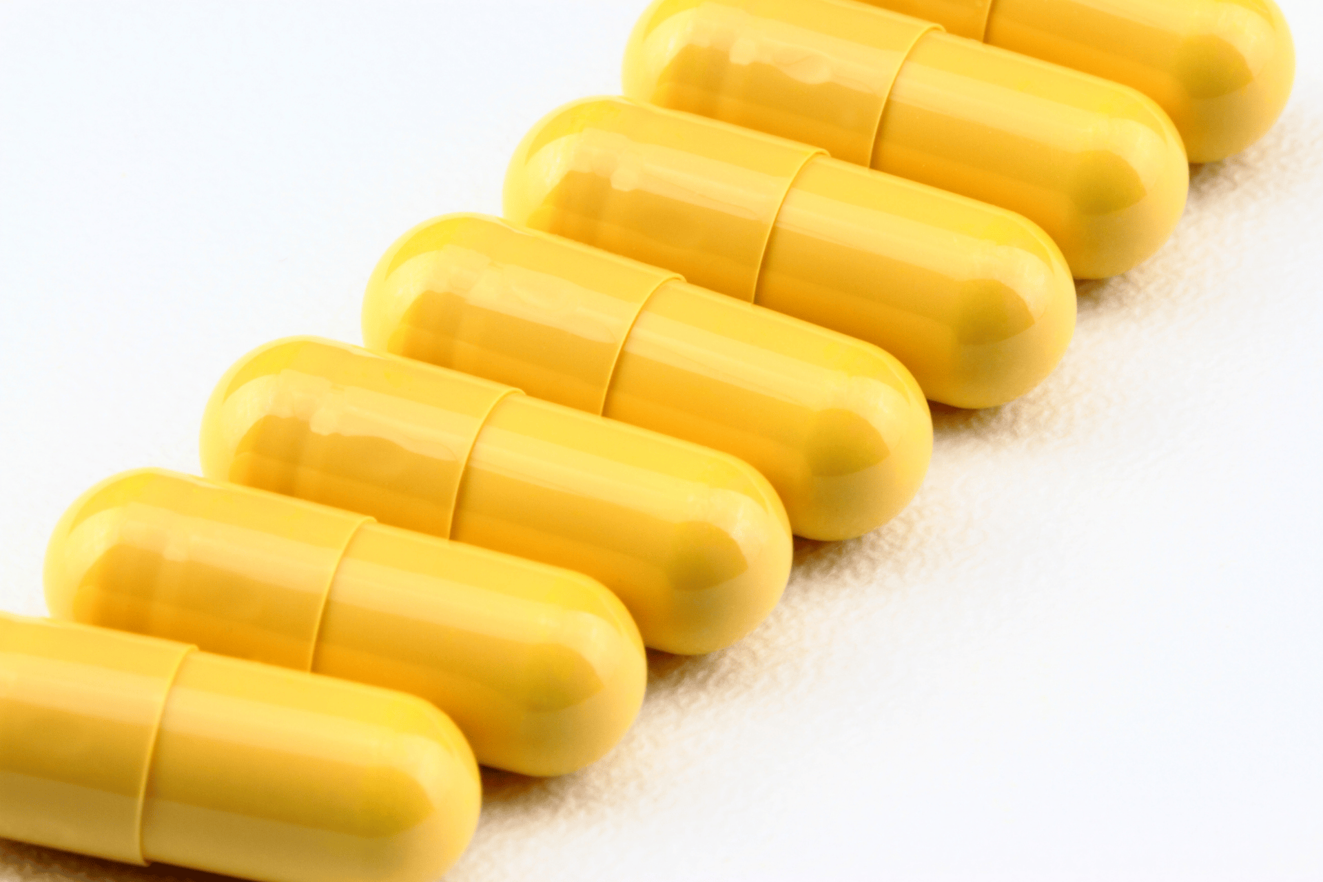 Close-up of several yellow capsules lined up in a diagonal row on a white surface.