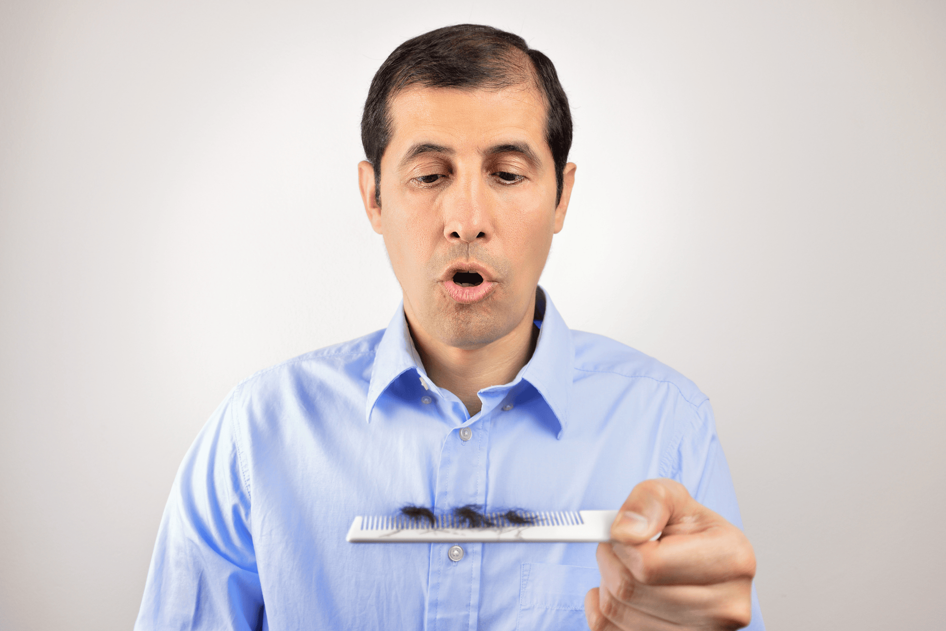 A Man looking surprised at a comb filled with fallen hair.