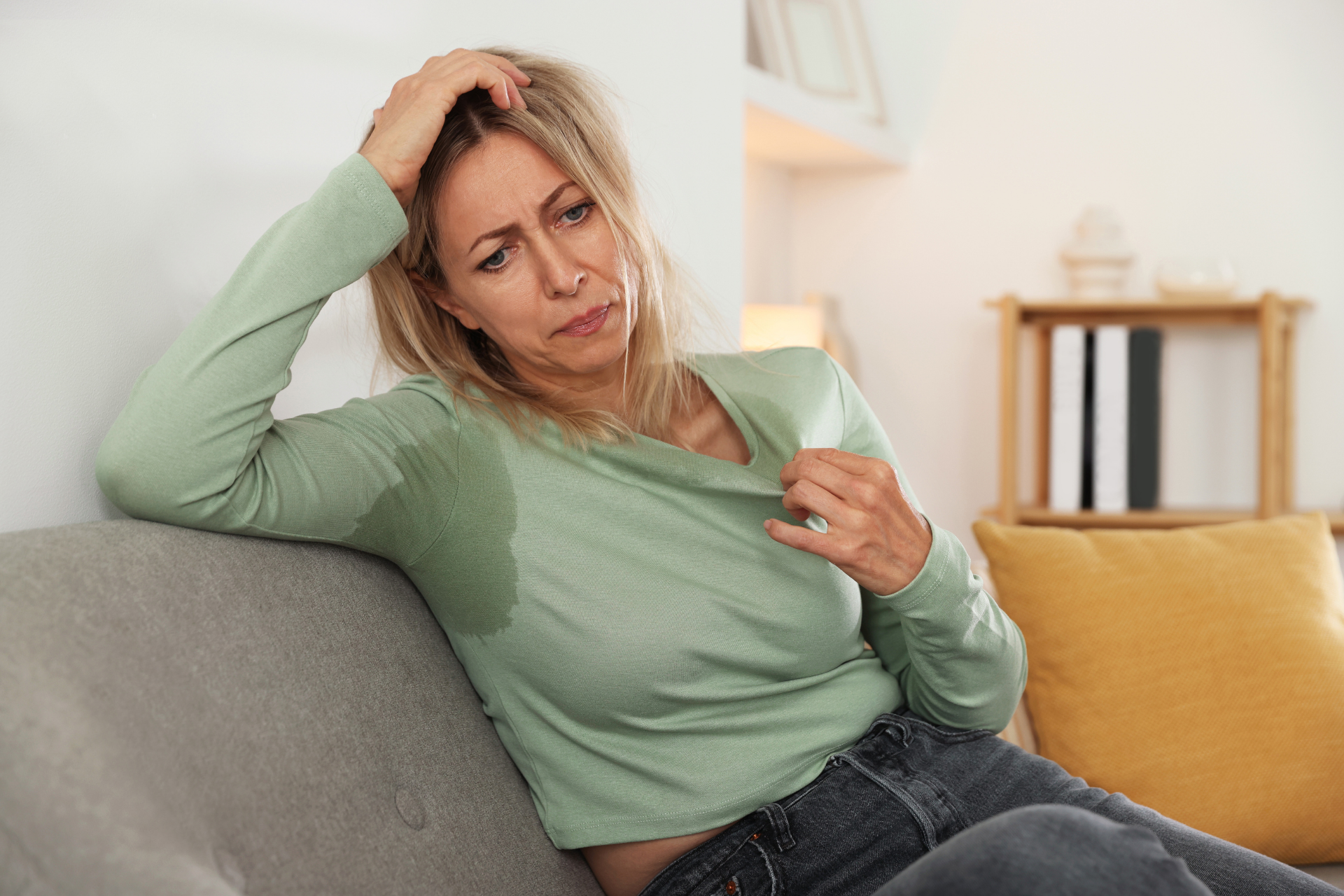 Woman sitting on a couch looking distressed, with large sweat stains under her arms.