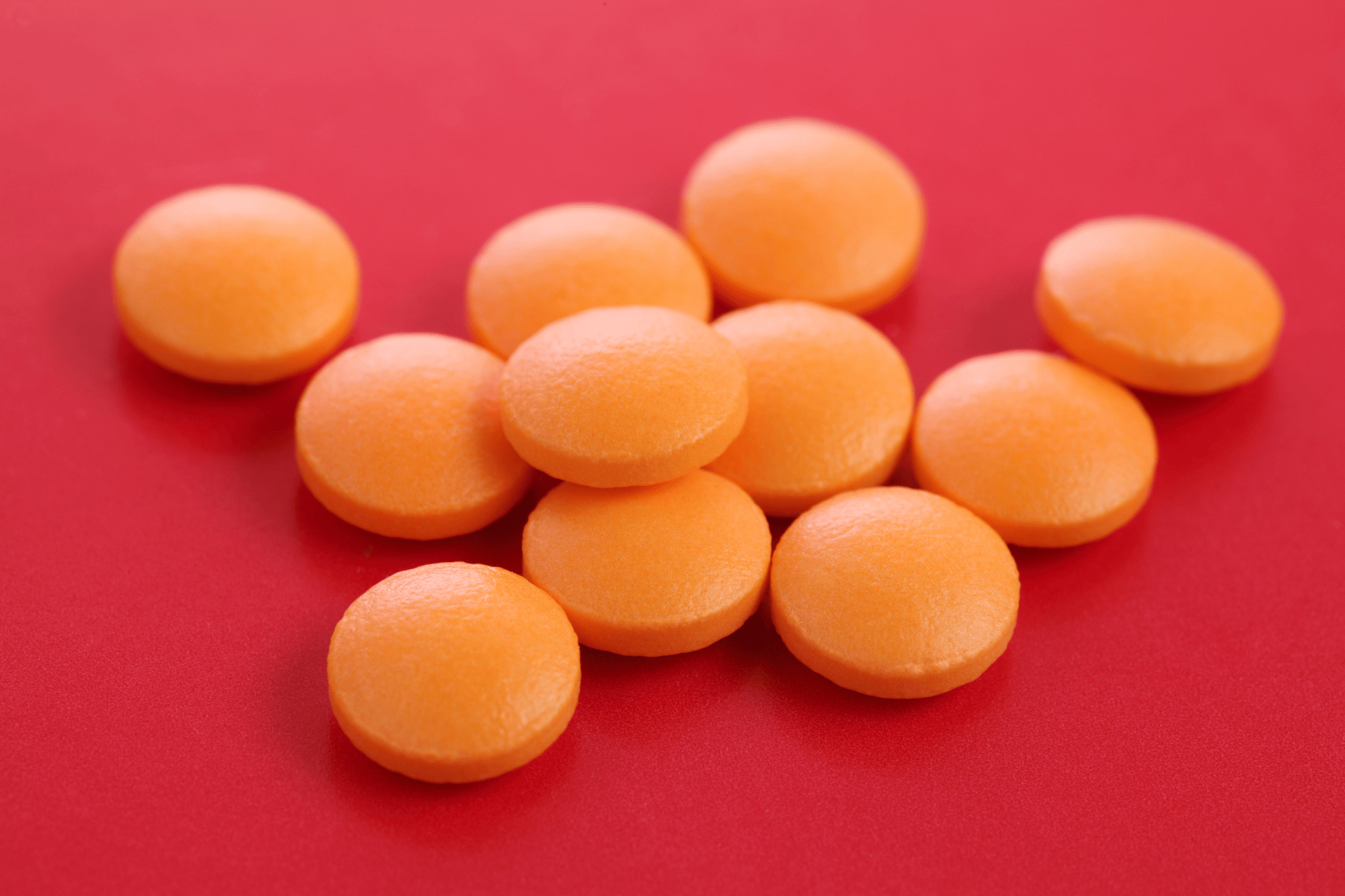 Round orange tablets scattered on a red surface.