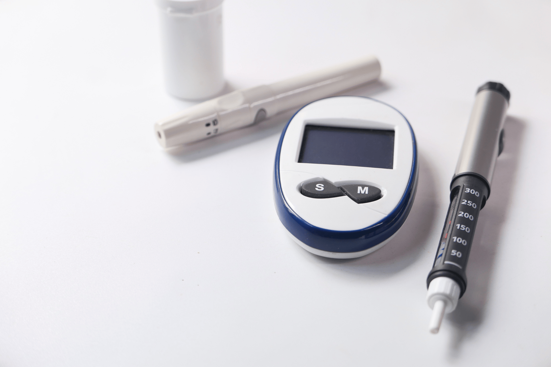 Diabetes supplies, including a glucose meter, lancet device, and insulin pen on a white surface.