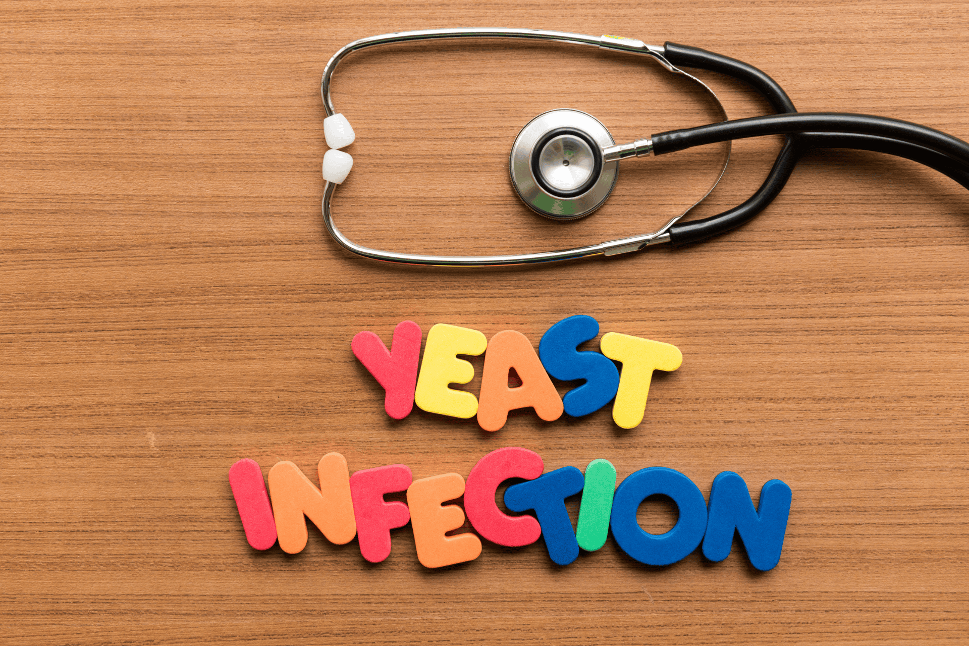 Colorful foam letters spelling “YEAST INFECTION” arranged on a wooden surface with a stethoscope placed above the text.