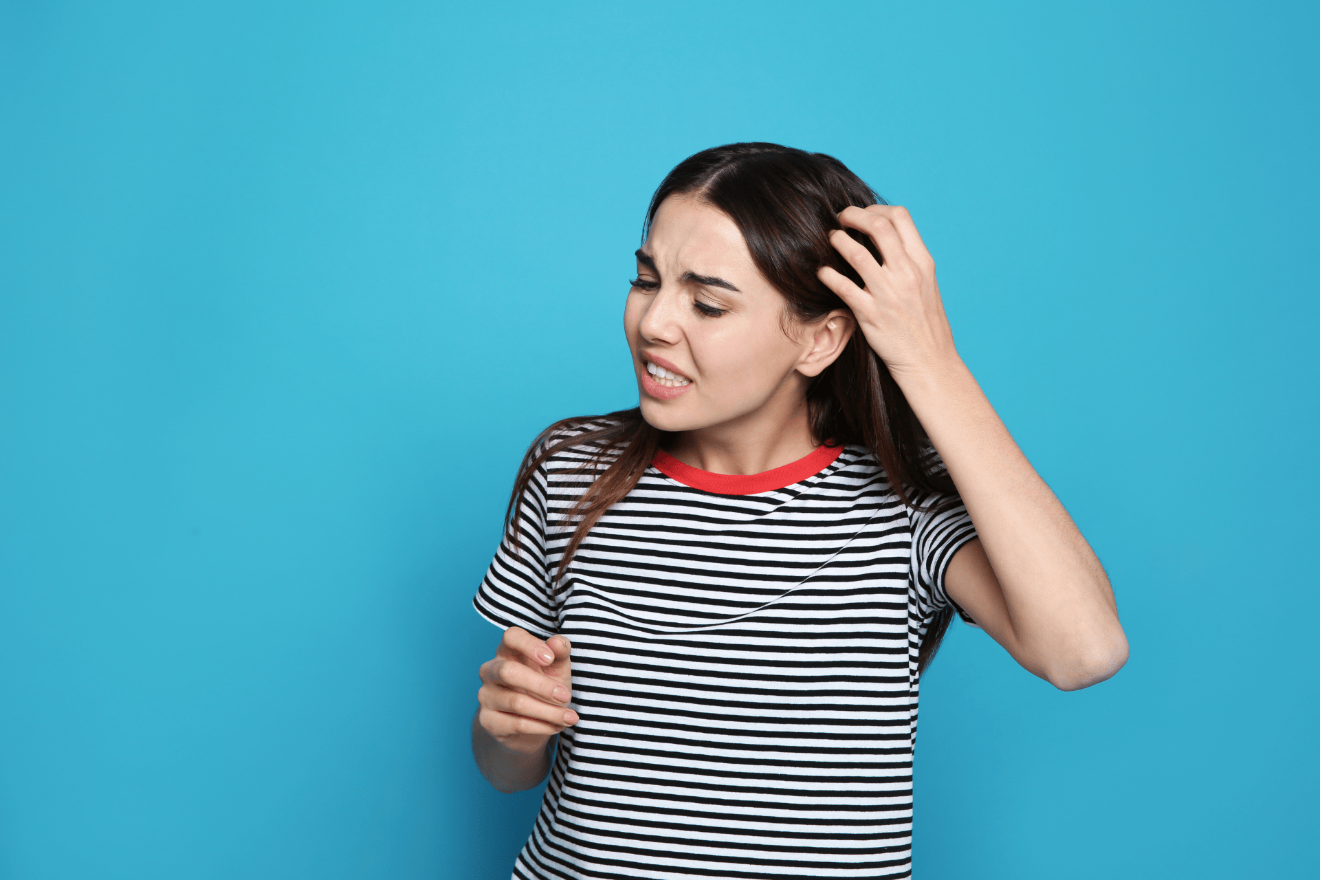 A woman scratching her scalp with a concerned expression against a blue background.