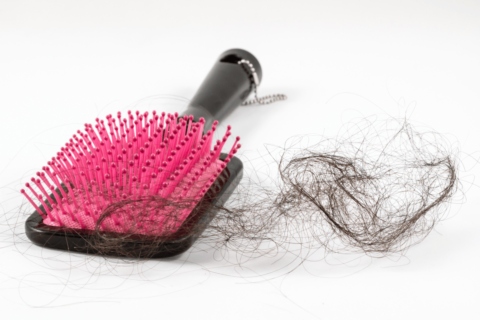 A hairbrush with strands of hair tangled in the bristles and loose hair beside it.