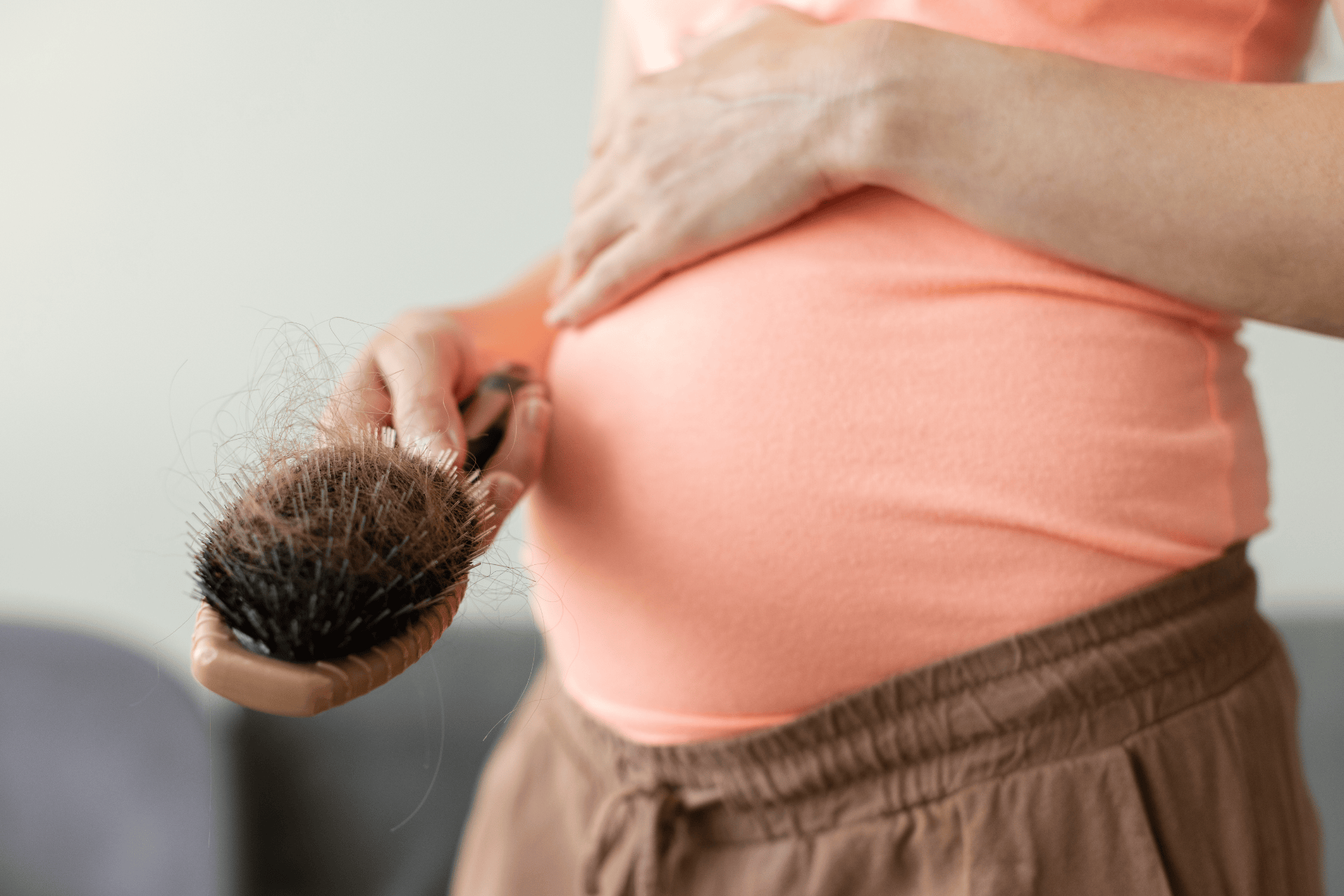 A person holding a hairbrush filled with shed hair while touching their midsection.