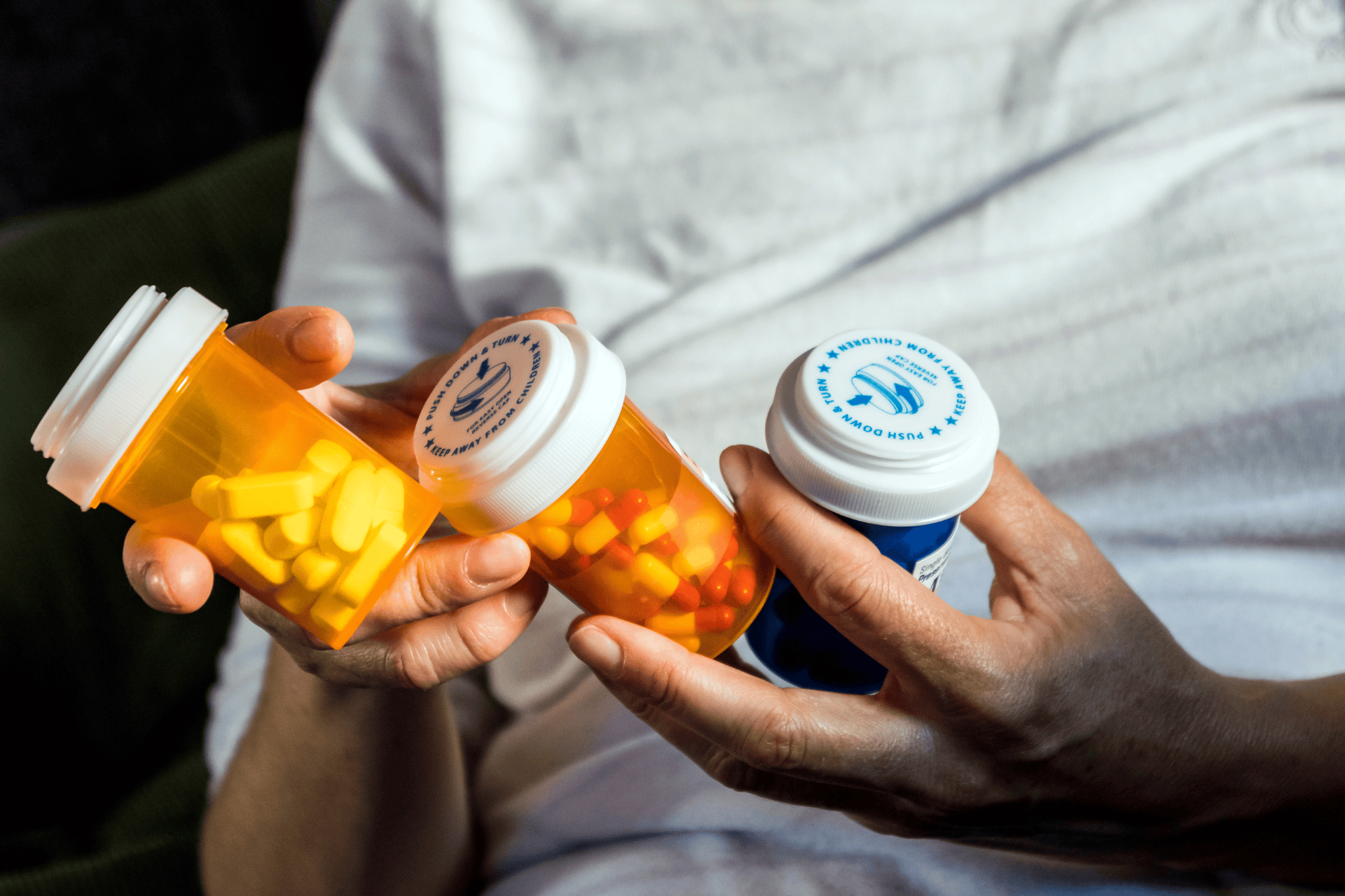 Person holding three prescription pill bottles with capsules and tablets