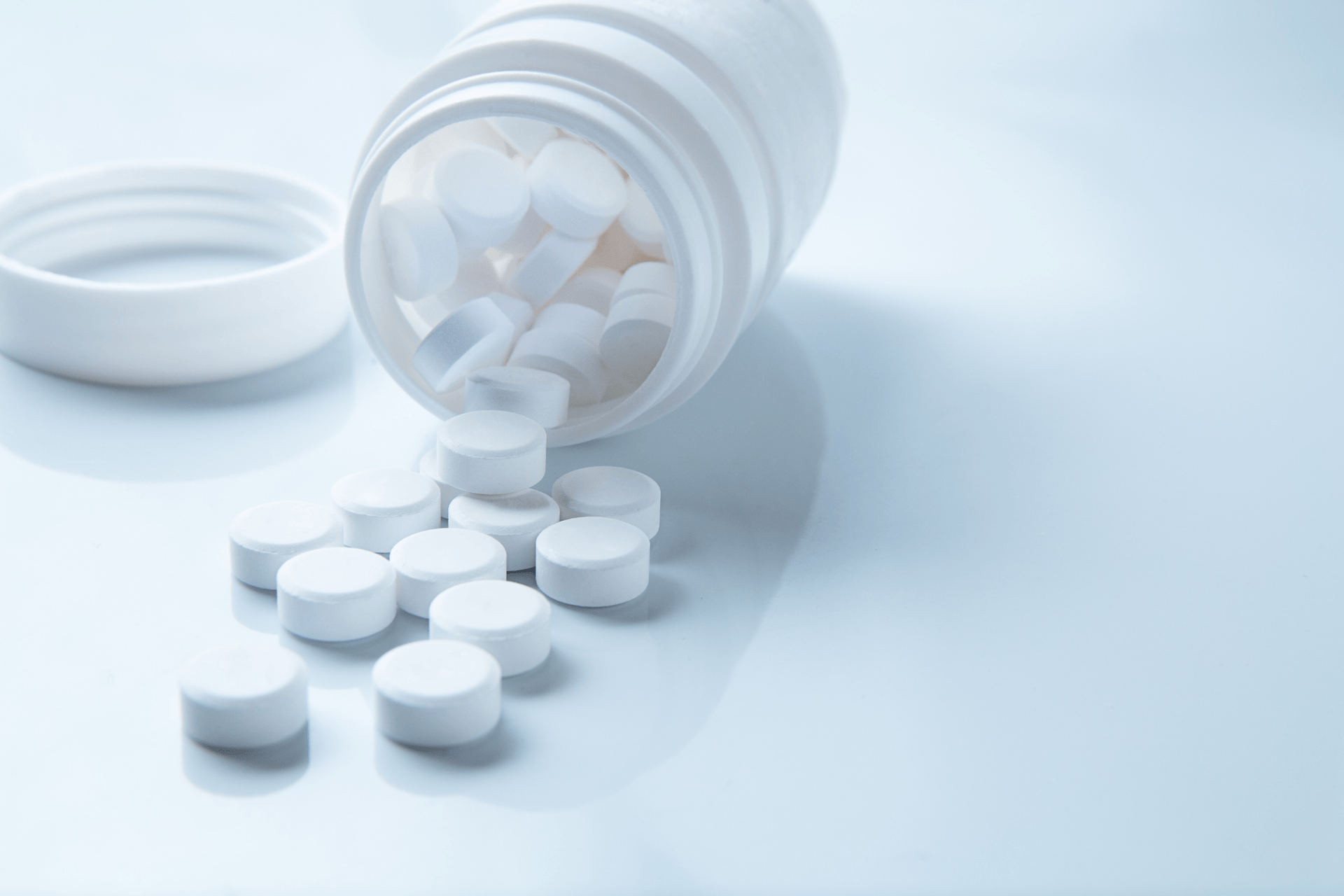 White pill bottle tipped over with round tablets spilling onto a clean surface.
