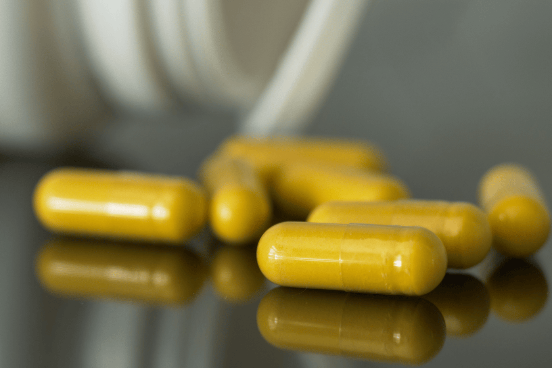 Yellow supplement capsules resting on a reflective surface.