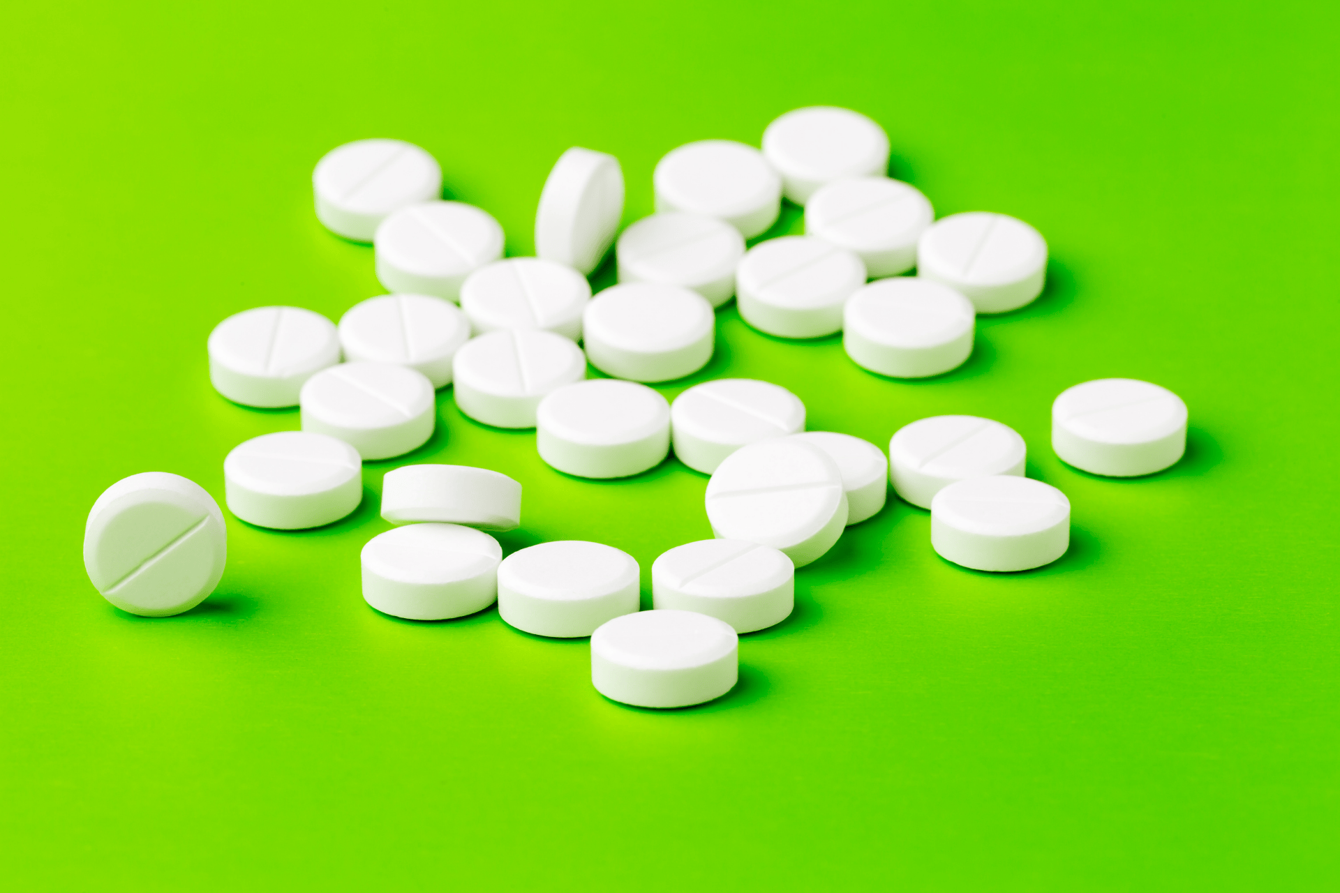 White round tablets scattered on a bright green background.