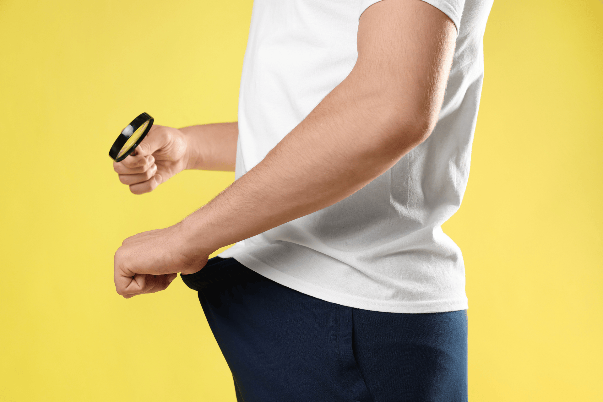 Man pulling out an empty pocket while holding a magnifying glass against a yellow background.