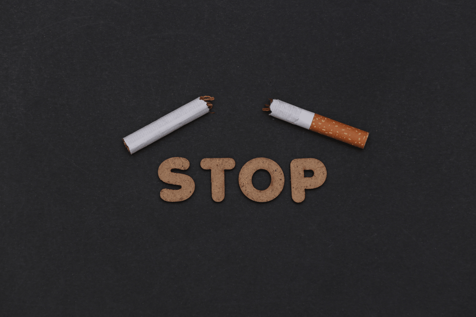 Broken cigarette above the word “STOP” on a dark background.