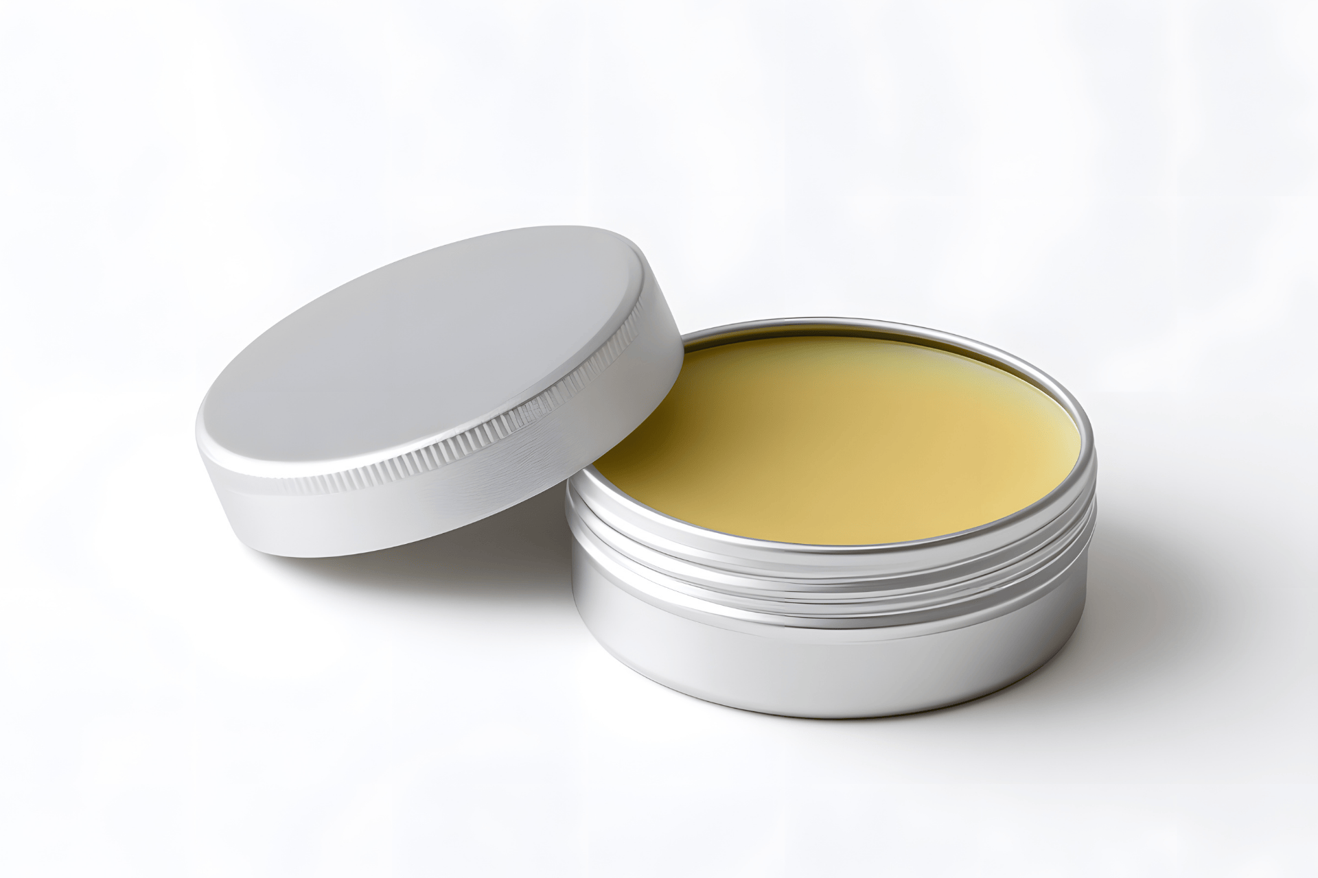 Open tin of medicinal ointment with a smooth yellow balm inside on a white background.
