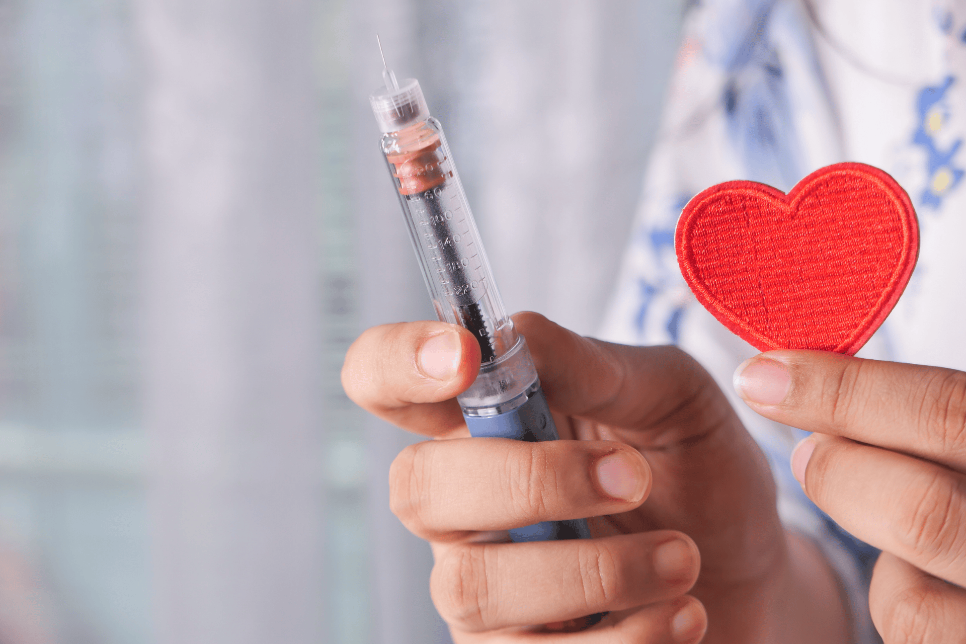 A close-up of a person holding a syringe in one hand and a small red fabric heart in the other, symbolizing healthcare, compassion, or medical treatment related to heart health.