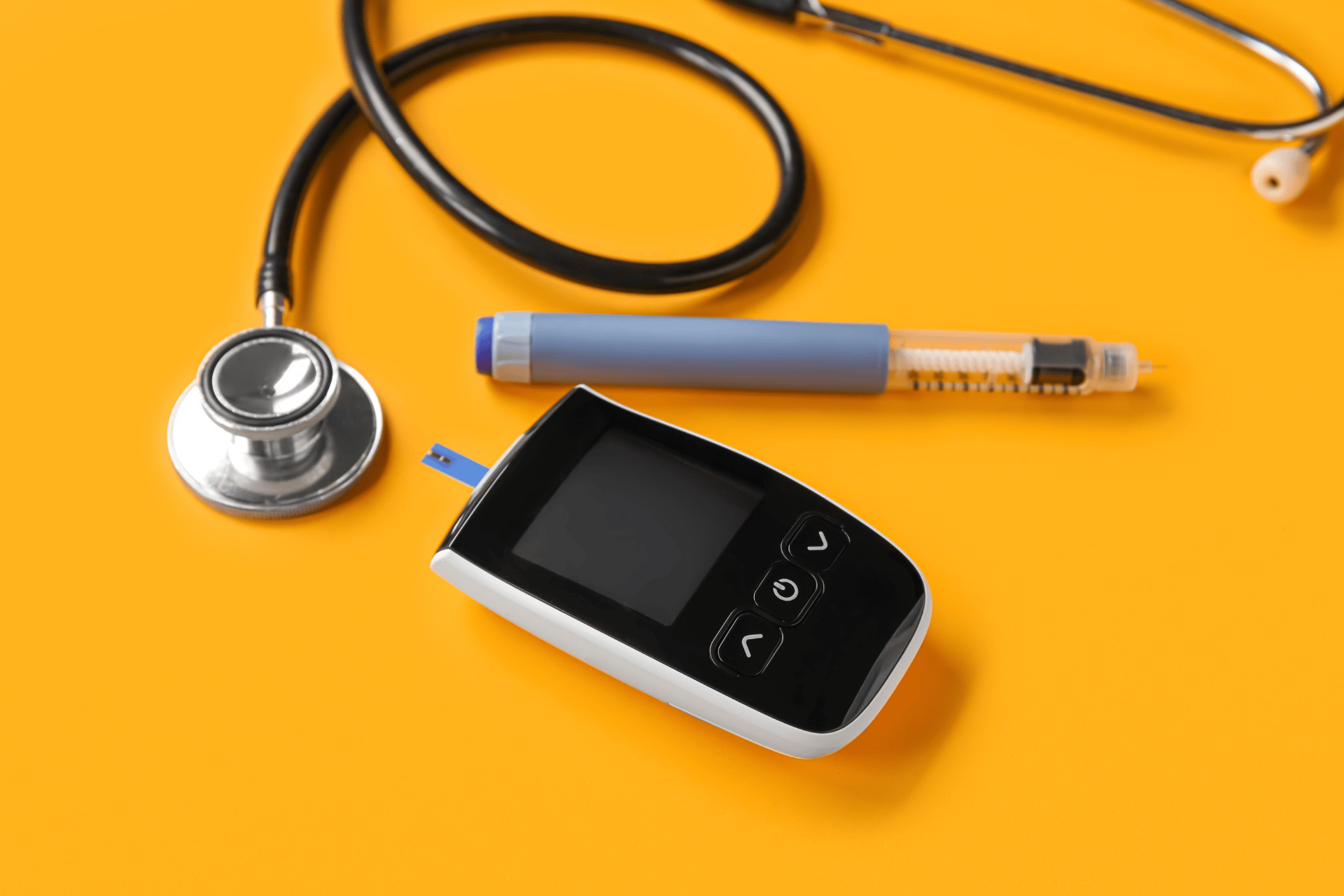 A blood glucose meter, stethoscope, and insulin pen on a yellow background.