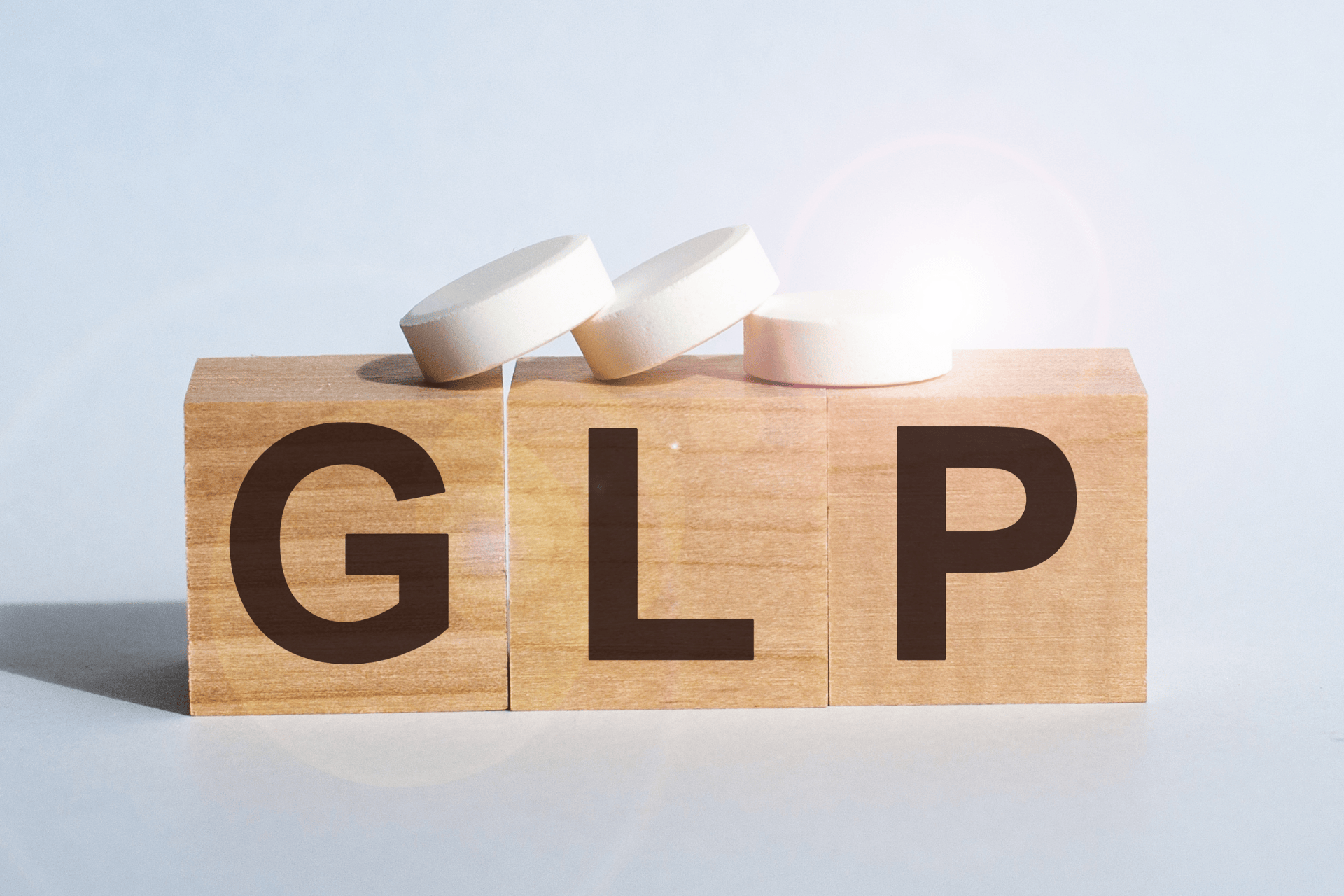 Three wooden blocks spelling “GLP” with white tablets on top.