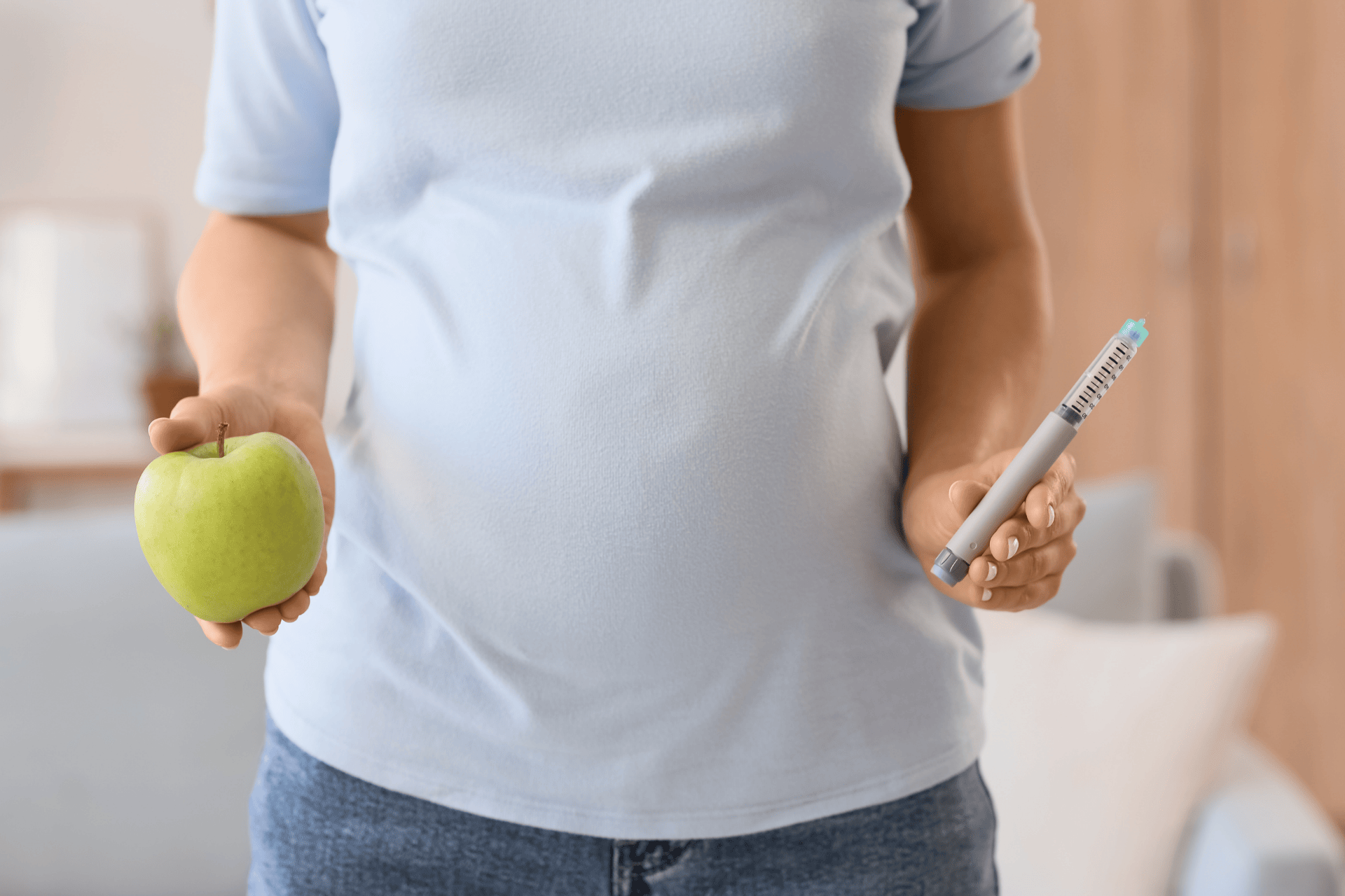 Person holding a green apple in one hand and an insulin pen in the other.
