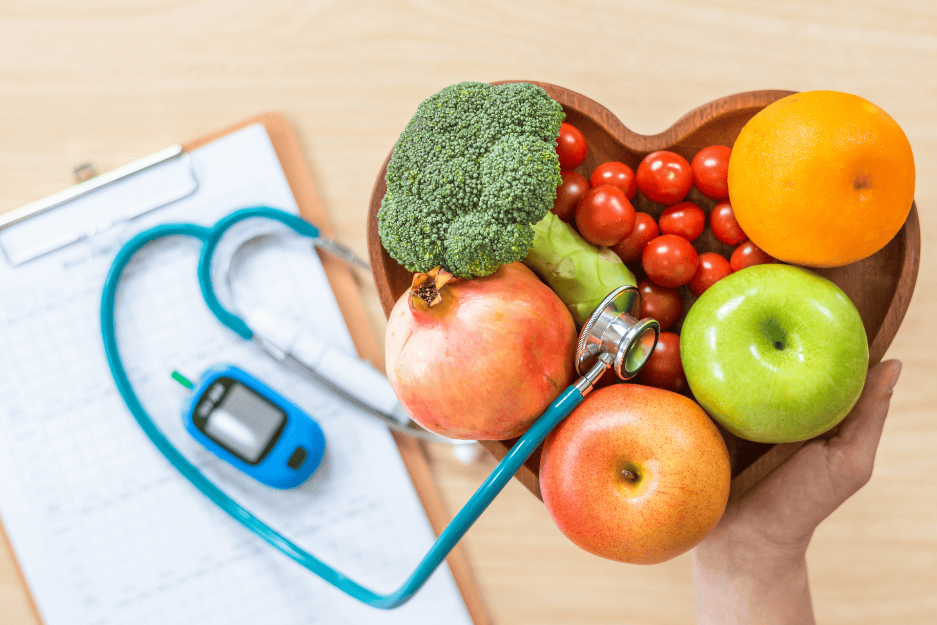 A heart-shaped bowl of fruits and vegetables with a stethoscope and glucose meter, symbolizing healthy nutrition and heart health.