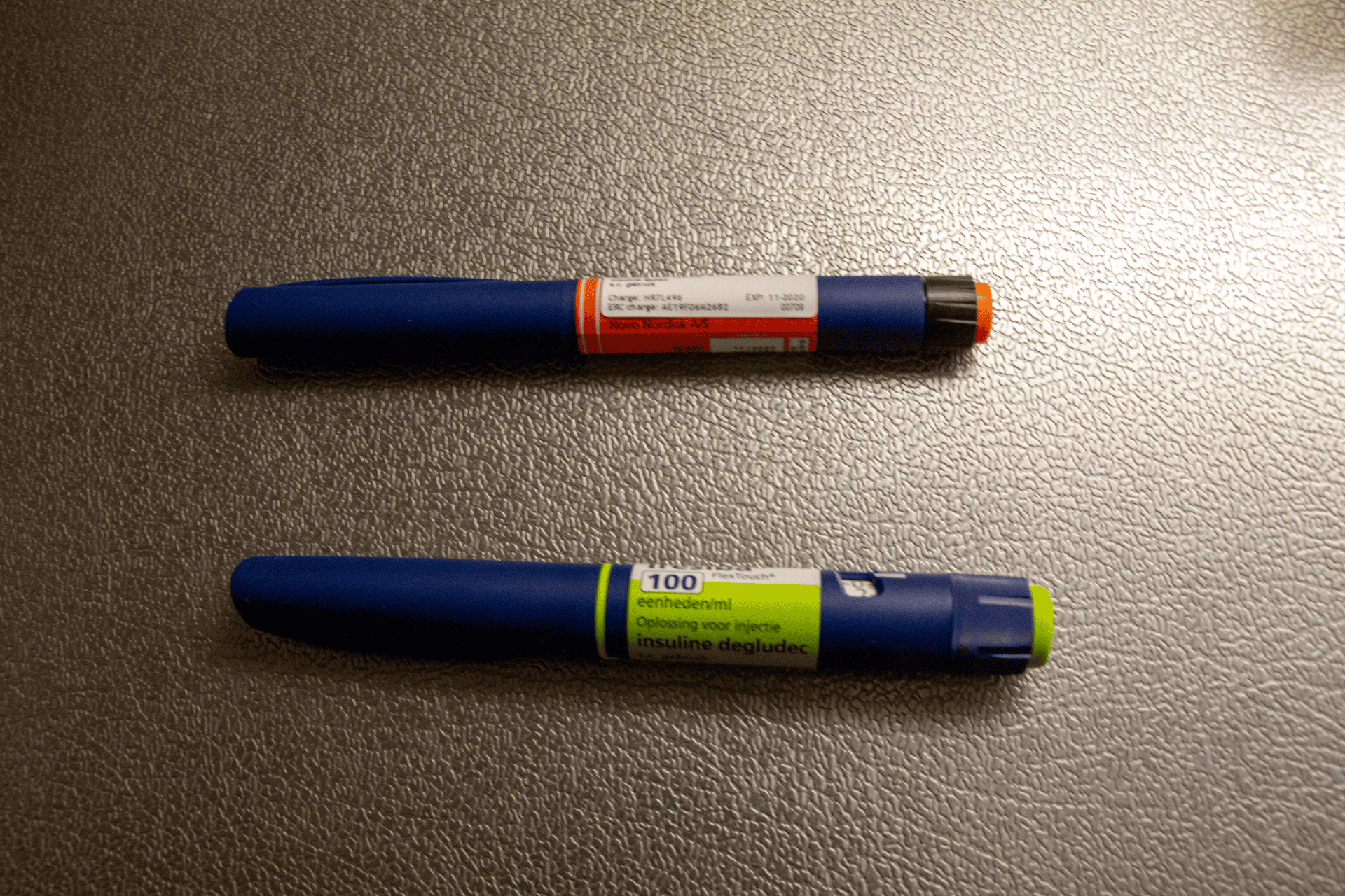Two insulin pens placed side by side on a textured surface.