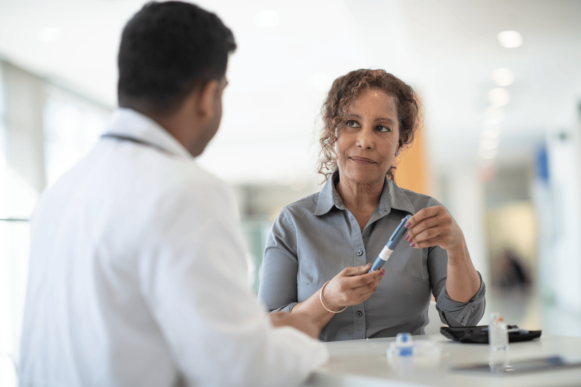 A woman holding an insulin pen while talking with a healthcare professional in a clinical setting.