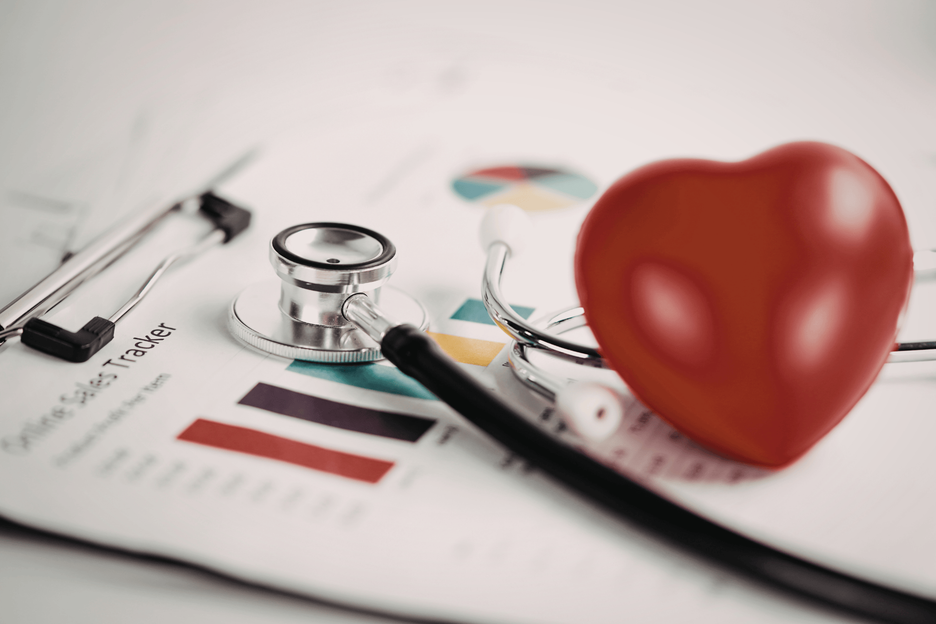 Stethoscope and red heart model resting on a health tracking chart with graphs.