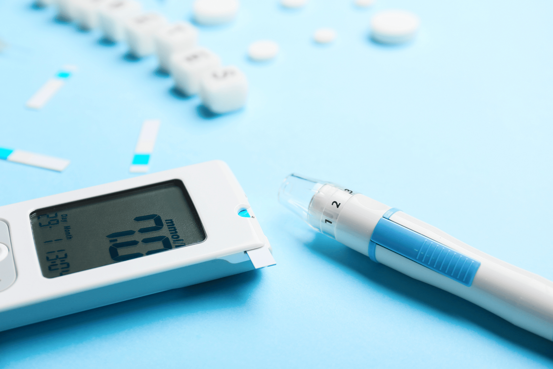 Blood glucose meter showing a reading next to an insulin pen and test strips on a light blue surface.