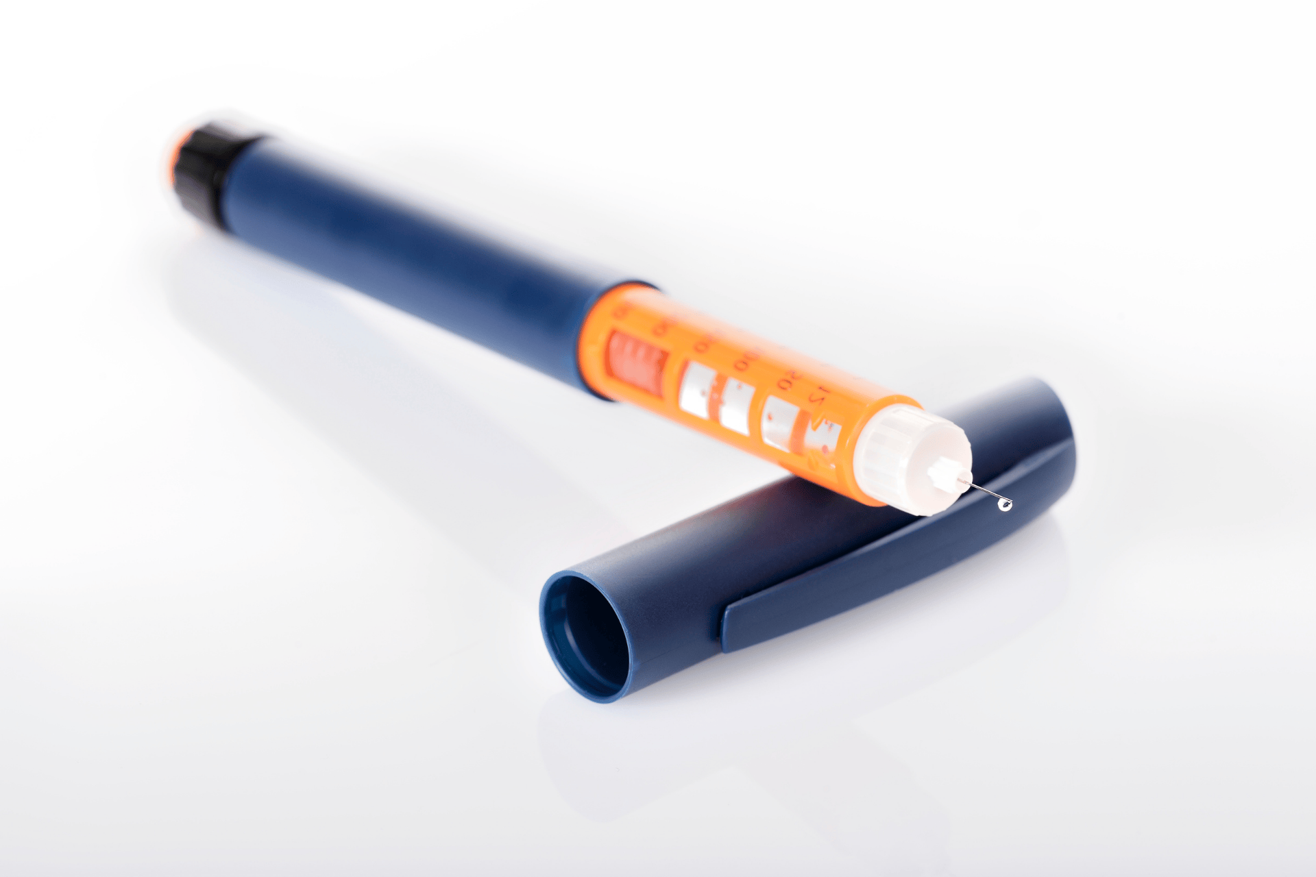 Insulin pen with an exposed needle and removable cap placed on a white surface.