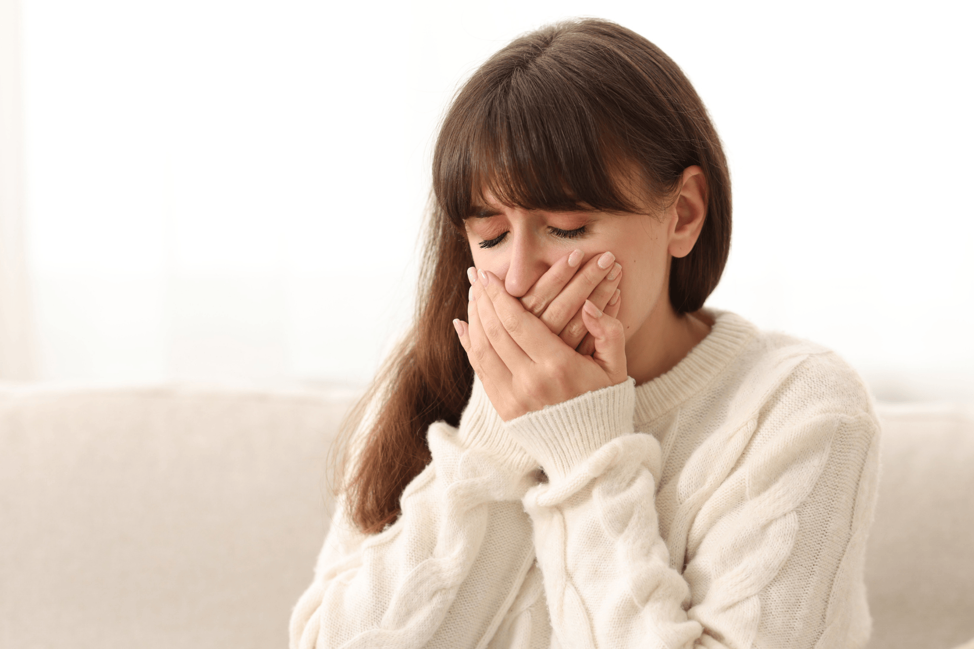 A woman covering her mouth, appearing uncomfortable from nausea.