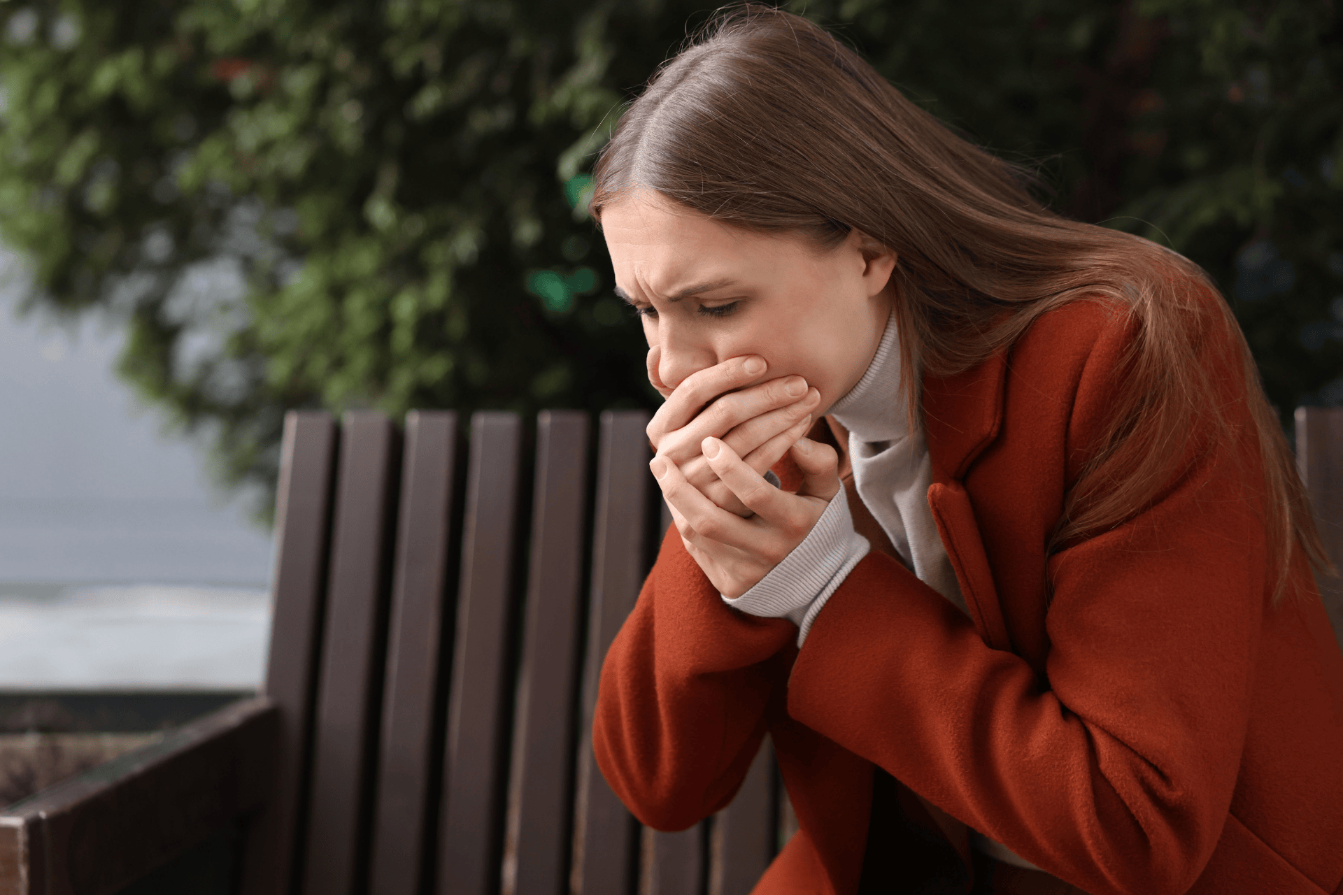 A woman outdoors covering her mouth, showing nausea and discomfort.