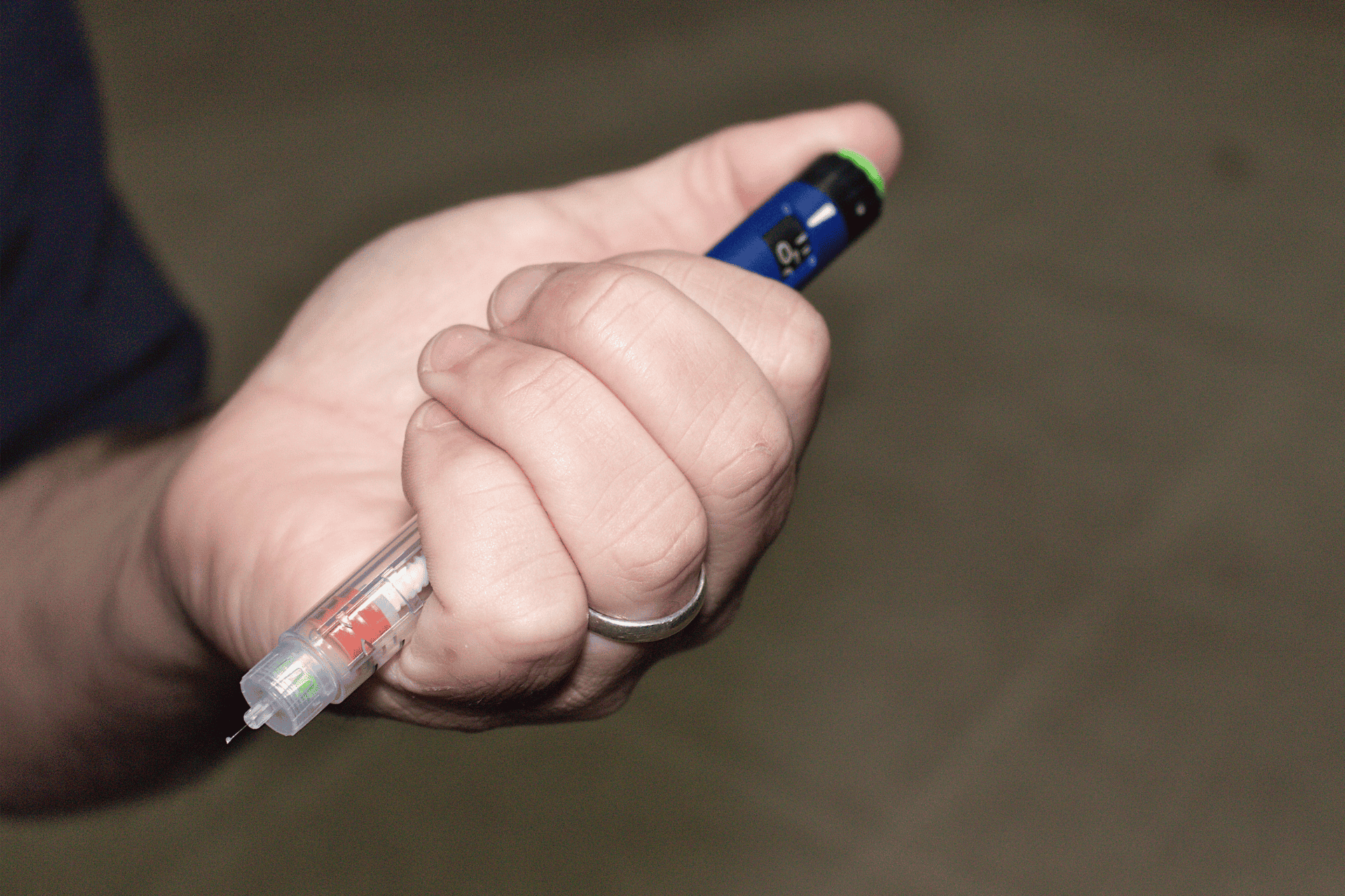 Hand holding an insulin pen prepared for injection.