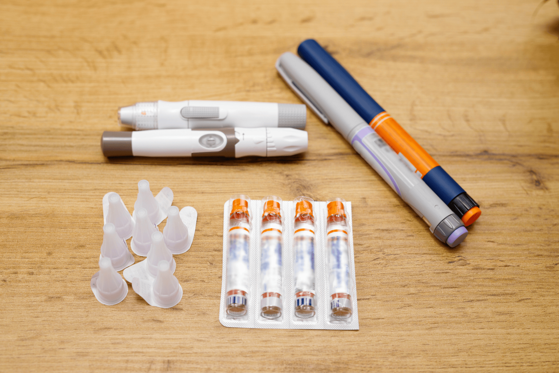 Diabetes supplies on a wooden surface, including insulin pens, pen needles, and disposable needle caps.