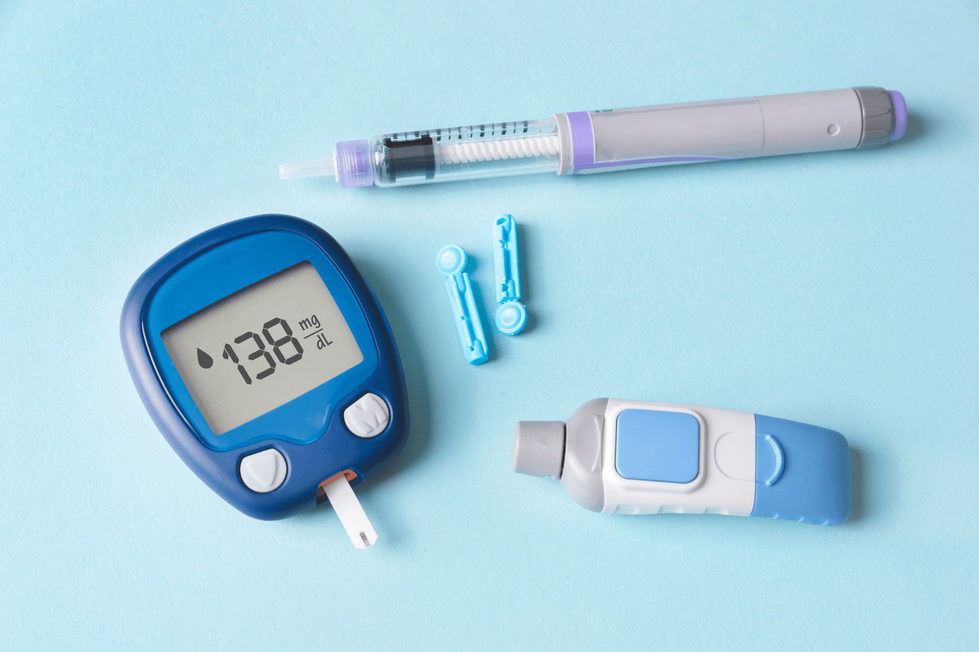 Blood glucose meter reading 138 mg/dL with insulin pen, lancets, and lancing device on a blue background.