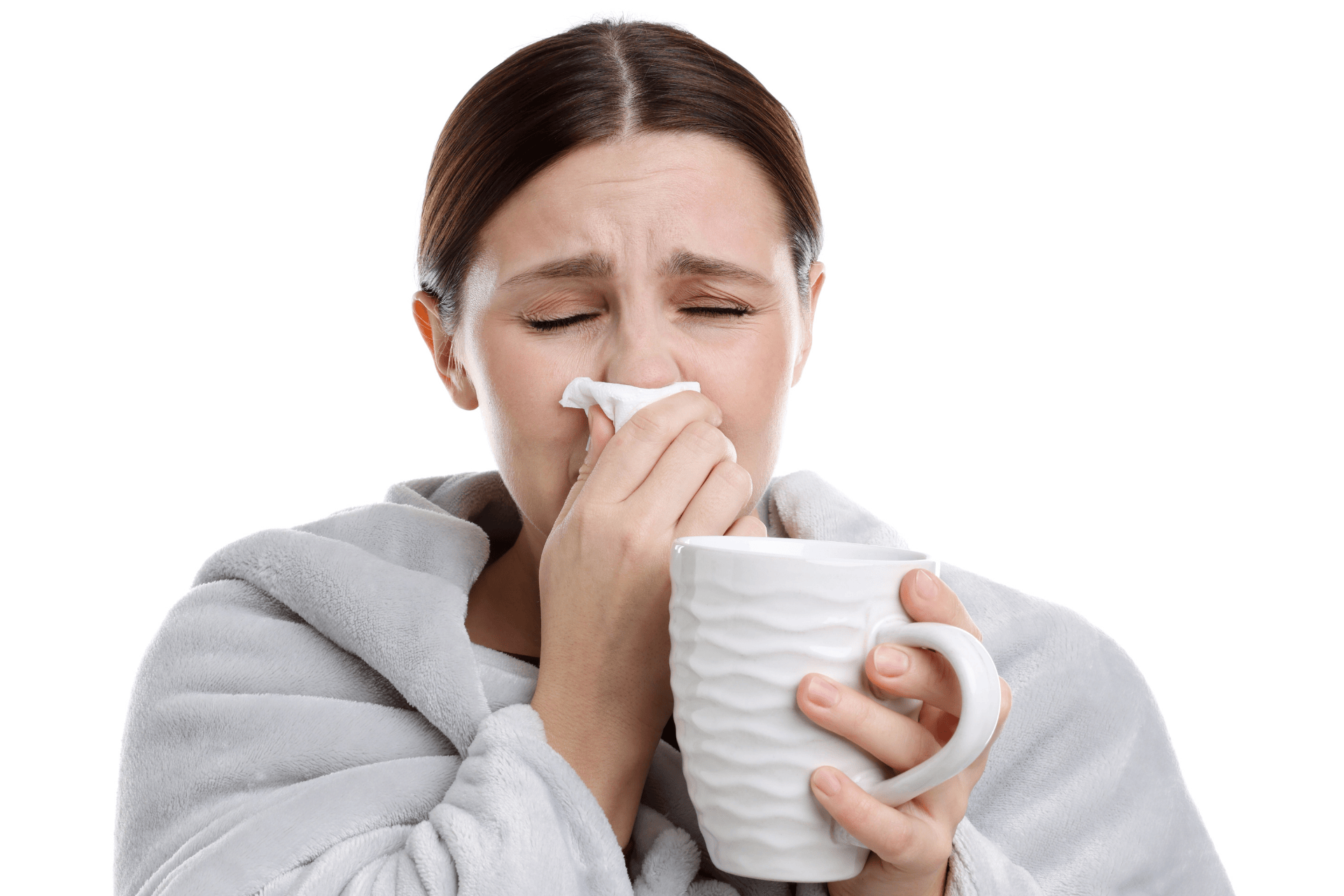Woman wrapped in a blanket holding a mug and tissue, showing symptoms of mucus and nasal congestion.
