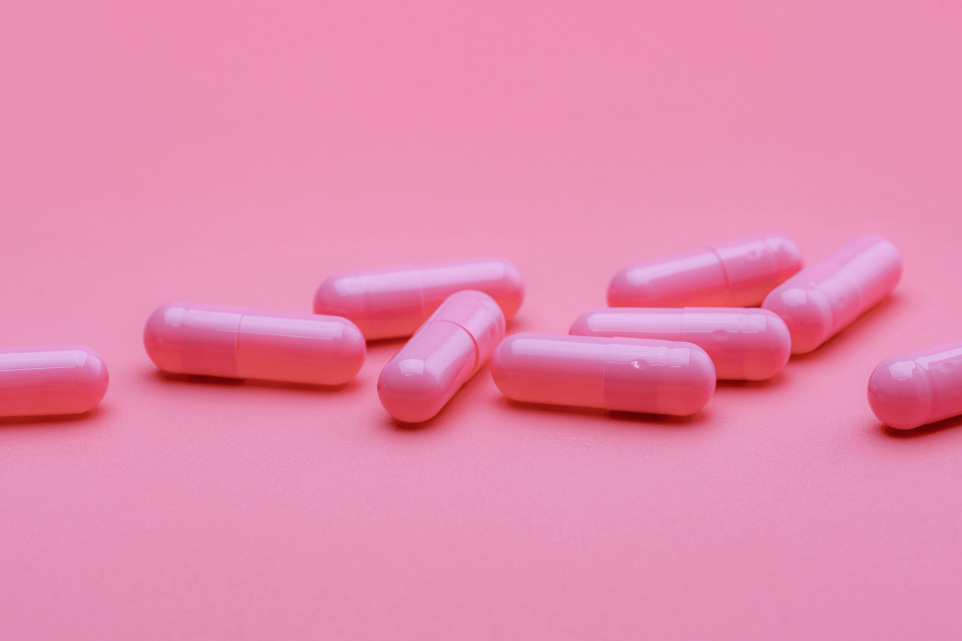 Pink capsules scattered on a pink background.