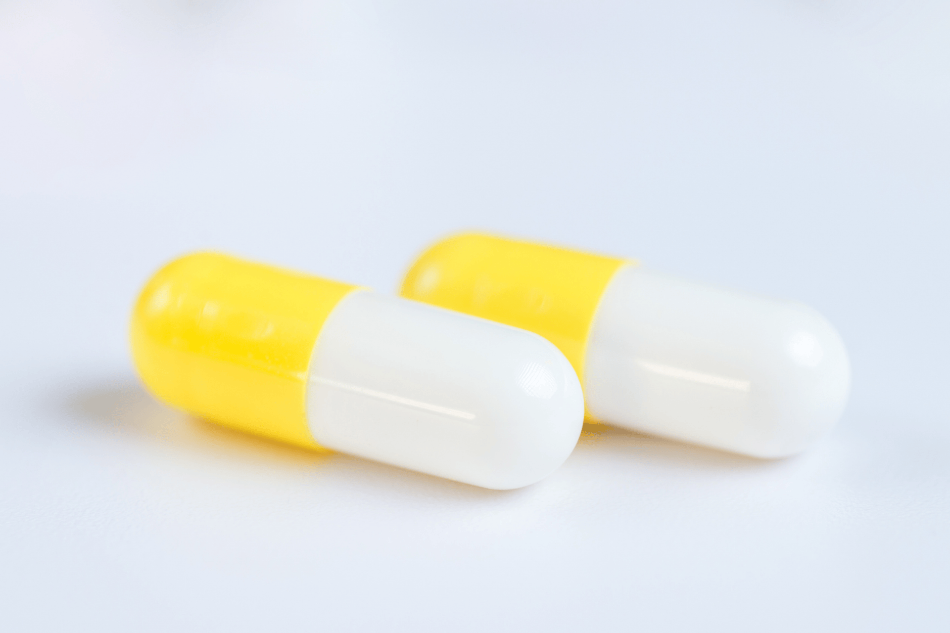 Two yellow-and-white capsules on a light background.