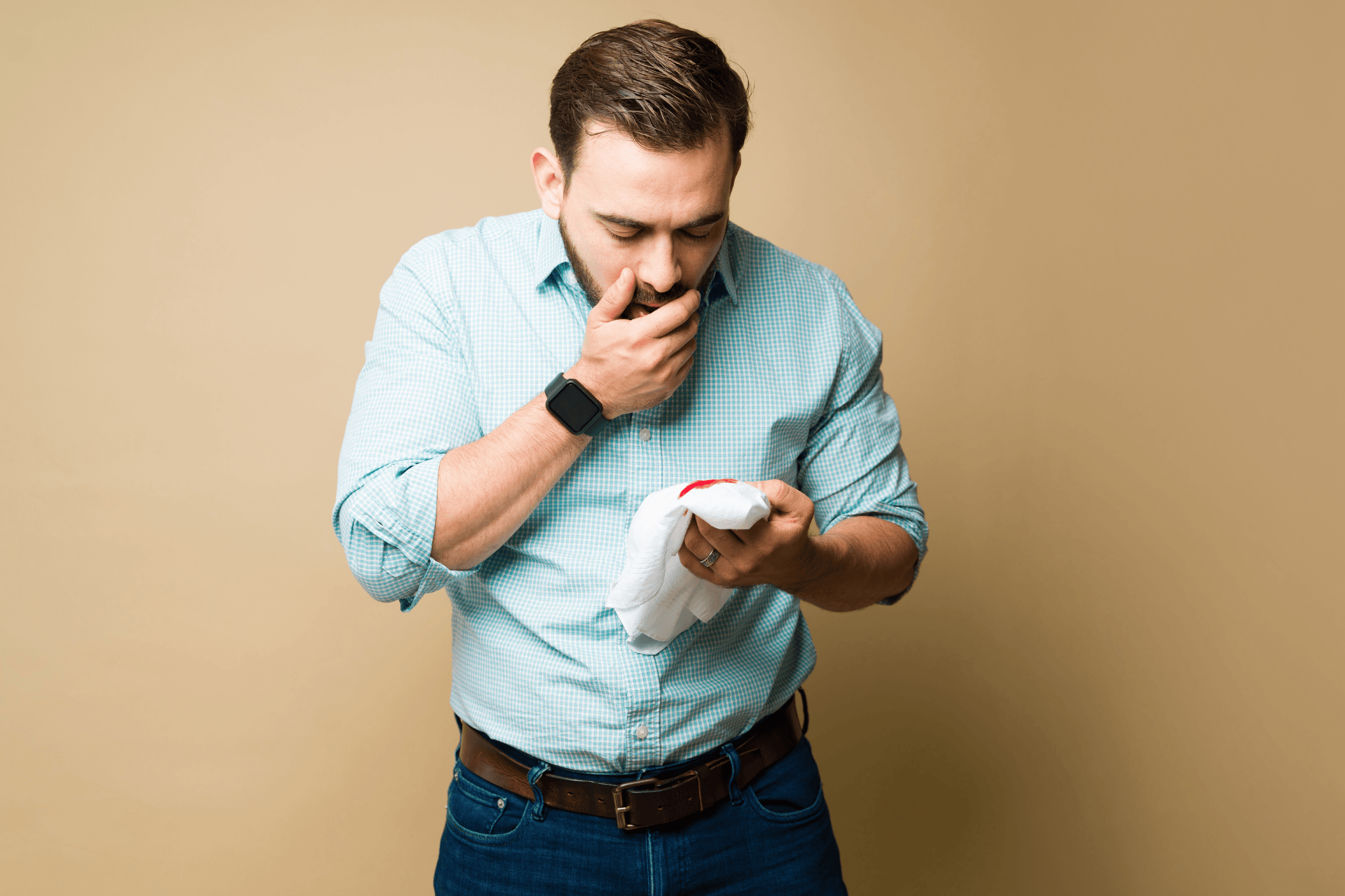 Man holding a tissue with blood while covering his mouth, appearing concerned about coughing up blood.