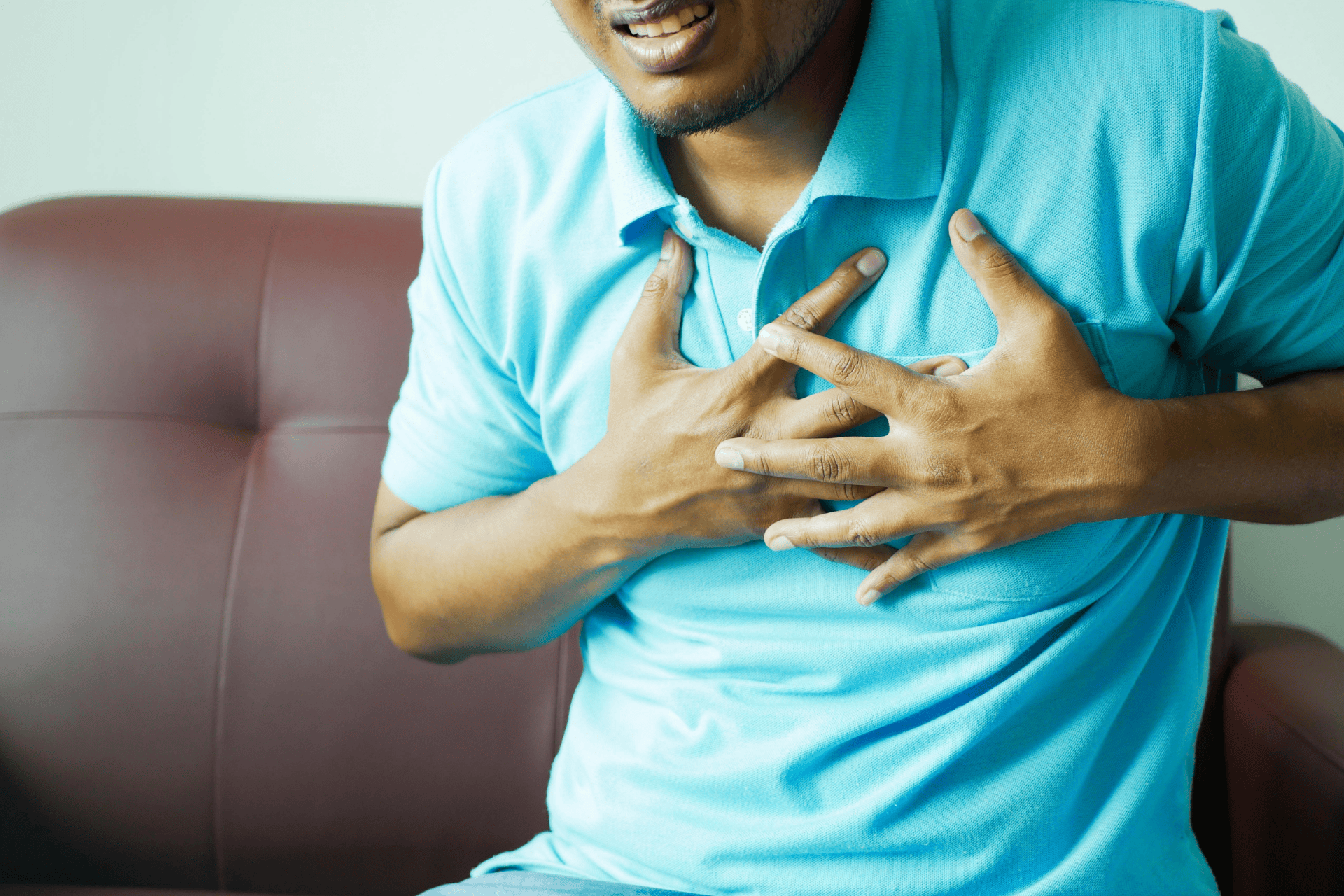 Man clutching his chest in pain while sitting on a couch.